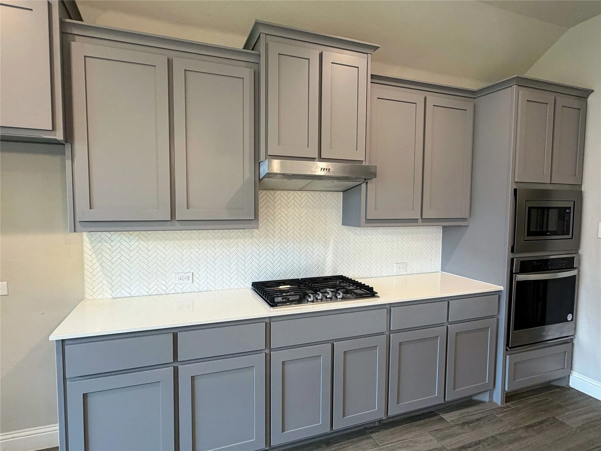 Kitchen featuring grey shaker-style cabinetry, white countertops, a white herringbone tile backsplash, stainless steel appliances, and wood-finish flooring