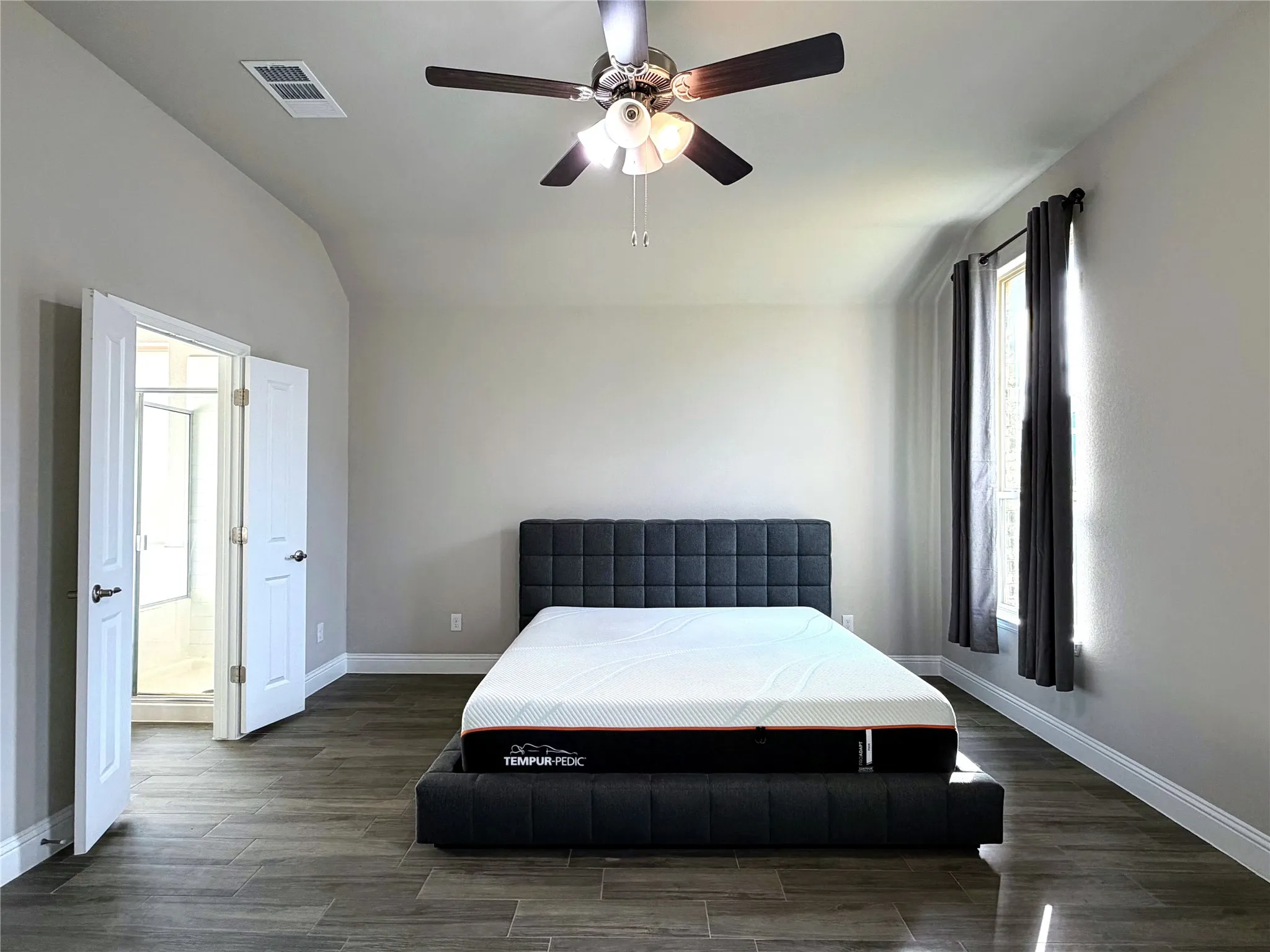 Vaulted ceiling with a ceiling fan, wood-finish flooring, and a window with drapery