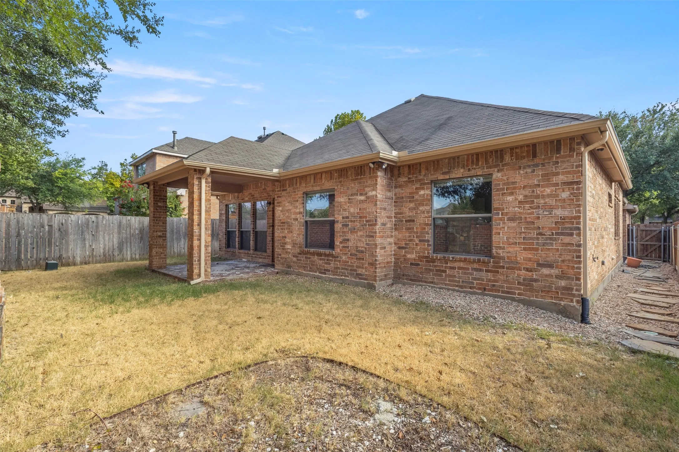 Brick exterior with covered patio, multiple windows, and a fenced yard