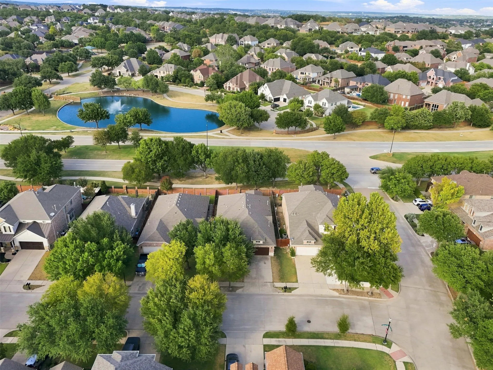 Residential neighborhood featuring an artificial pond, mature trees, and paved roads