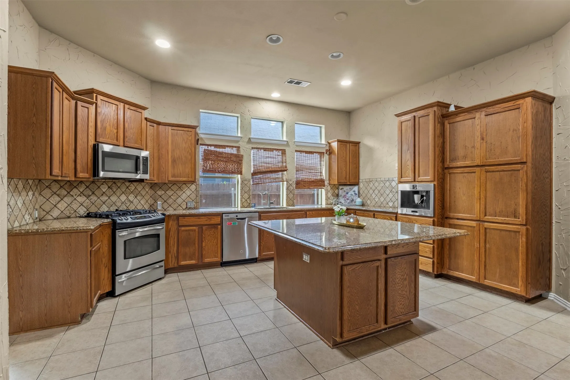 Kitchen featuring wood cabinetry, stainless steel appliances, built in Cappucino machine, a center island with a granite countertop, and tiled flooring
