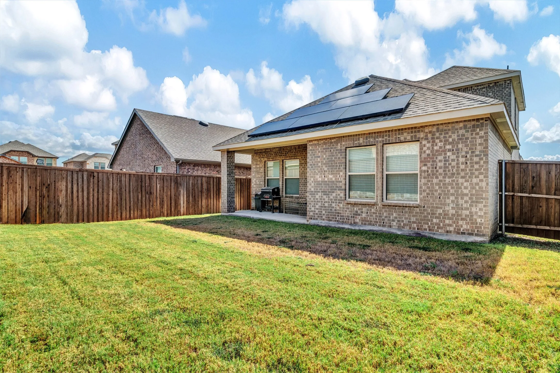 Rear view of property with solar panels, a yard, and a patio area