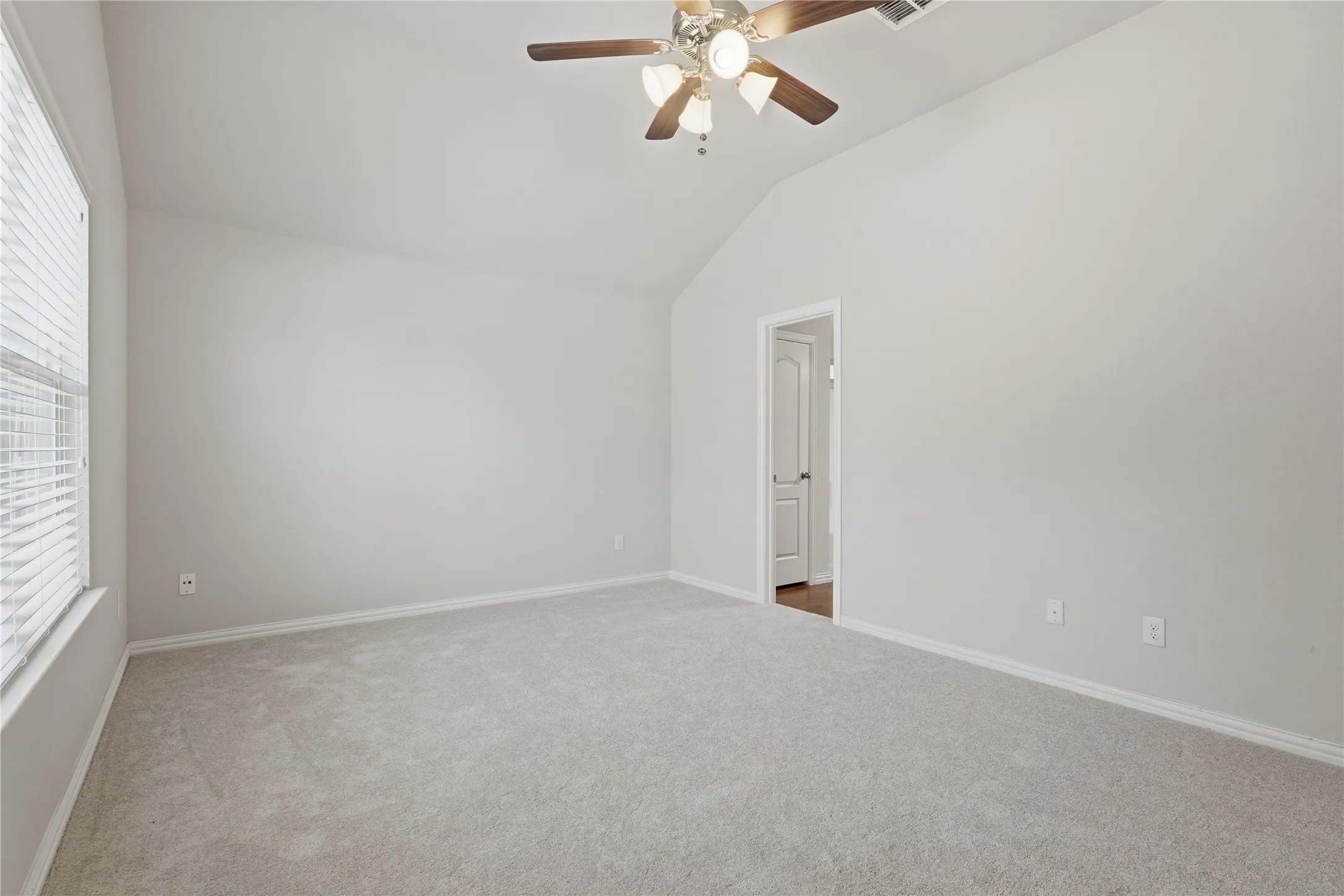 Vaulted ceiling, ceiling fan with light fixture, light grey carpeting, window with blinds, and white trim