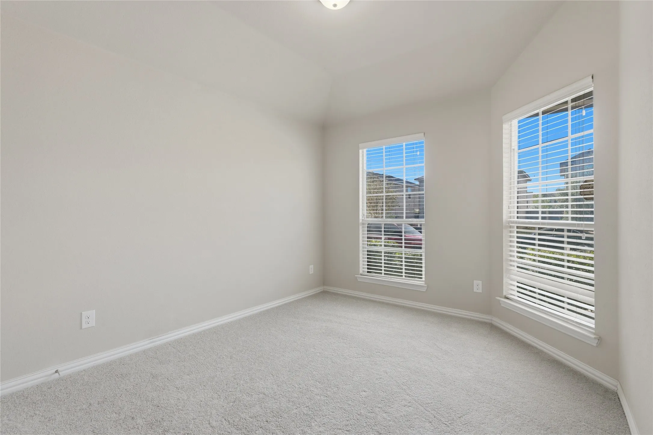 Recessed lighting, light gray carpeting, two large windows with blinds, and neutral wall paint