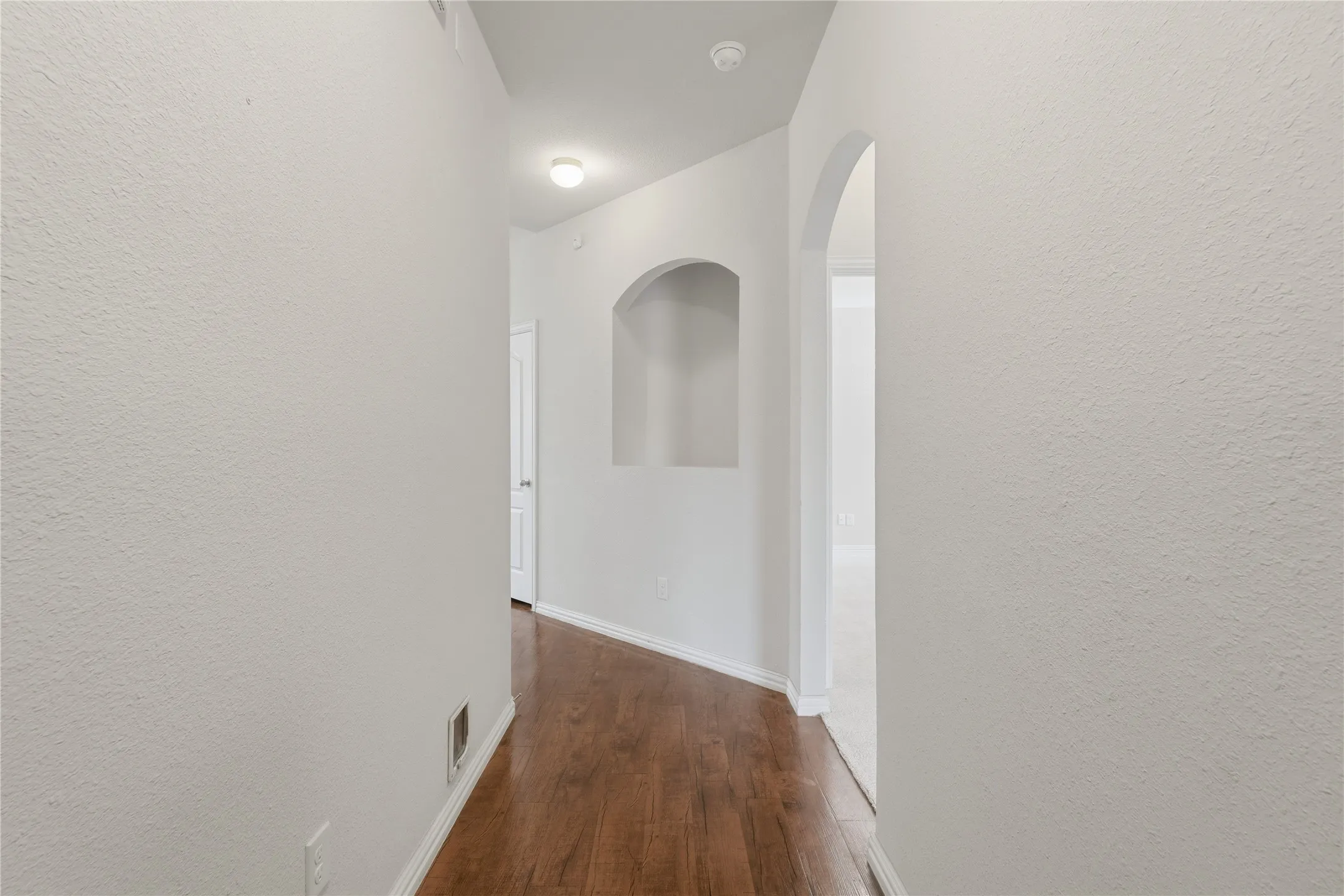 Hallway with wood-finish flooring, an arched doorway, a built-in wall niche, and white baseboards