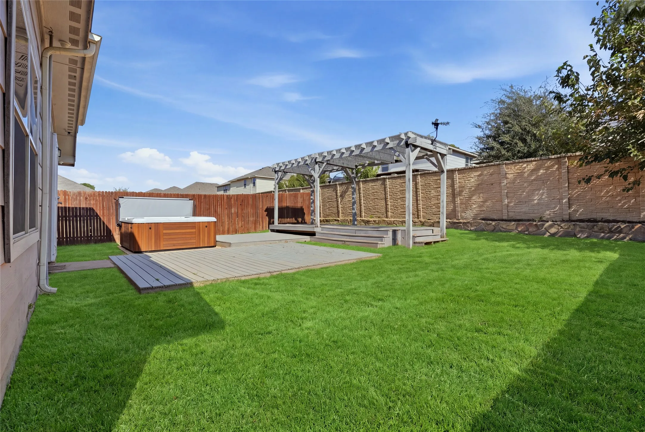 Expansive backyard featuring a manicured lawn, a wood pergola, and a built-in hot tub on a multi-level deck