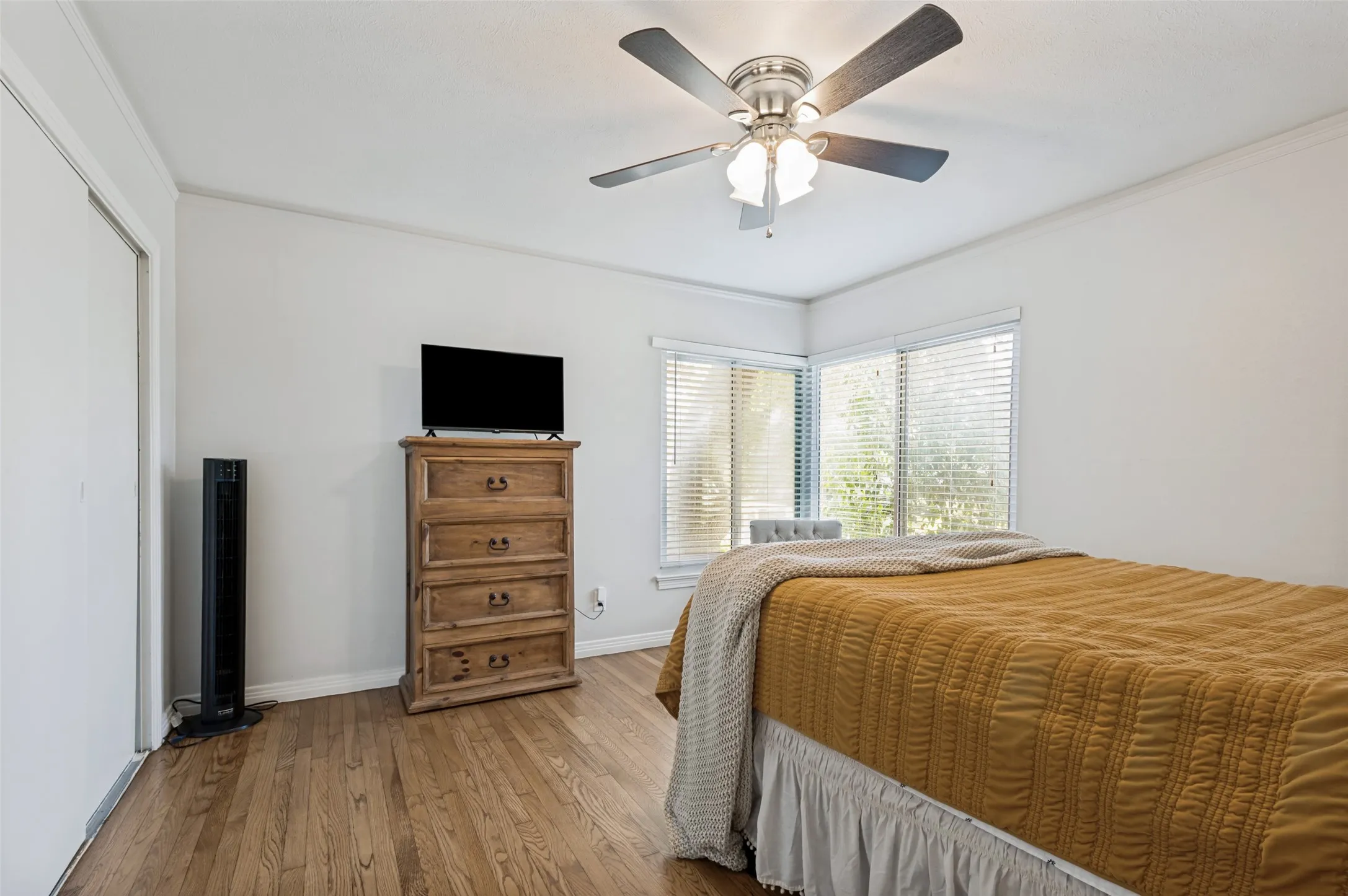 Hardwood flooring, corner windows with blinds, ceiling fan with integrated lighting, and white walls