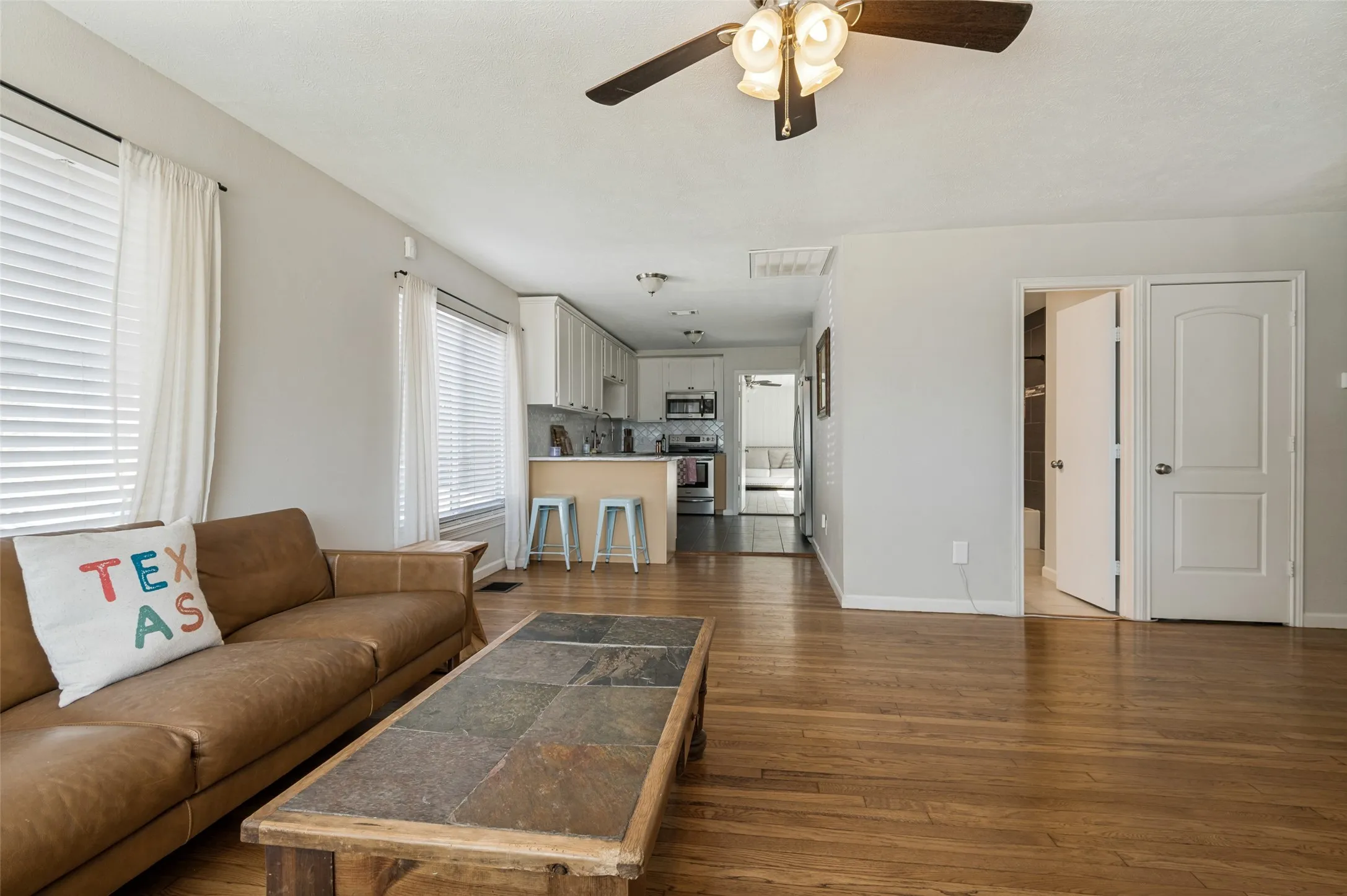 Wood-finish flooring throughout, ceiling fan with integrated lighting, recessed lighting, white window blinds, and white kitchen cabinetry