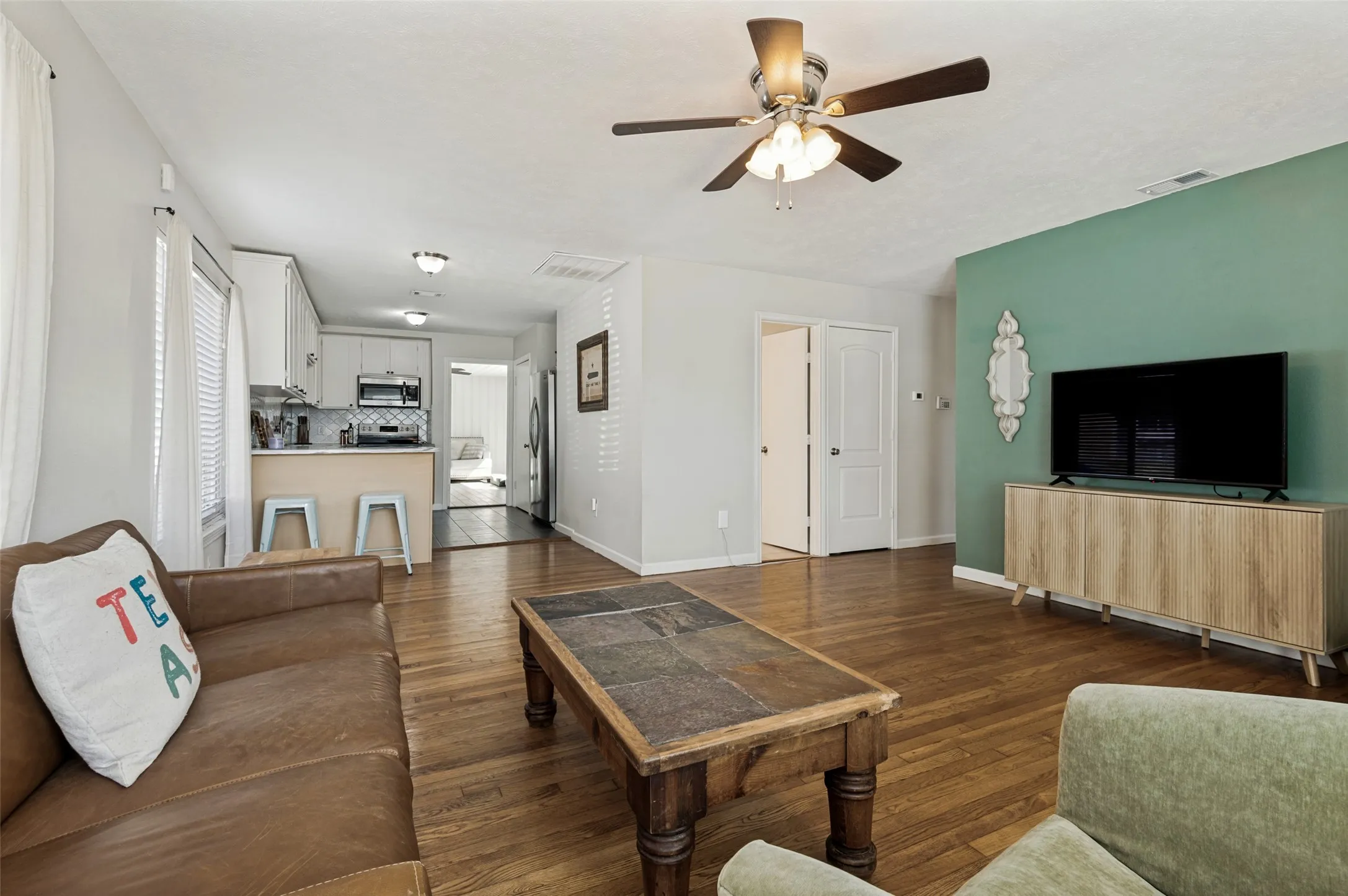 Hardwood-style flooring throughout, ceiling fan with integrated lighting, white kitchen cabinetry, stainless steel microwave, and white double doors