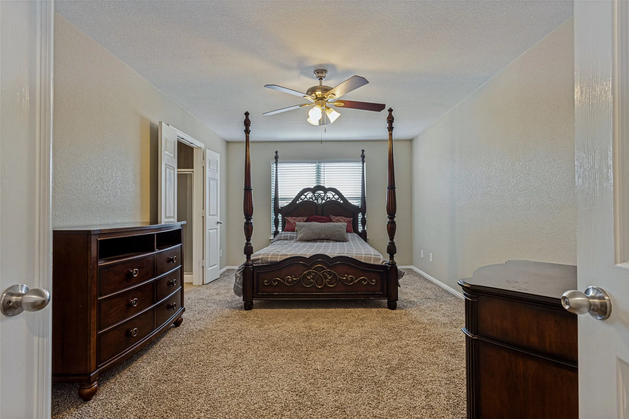Carpeted flooring, ceiling fan with integrated lighting, window with horizontal blinds, and a built-in closet with bi-fold doors