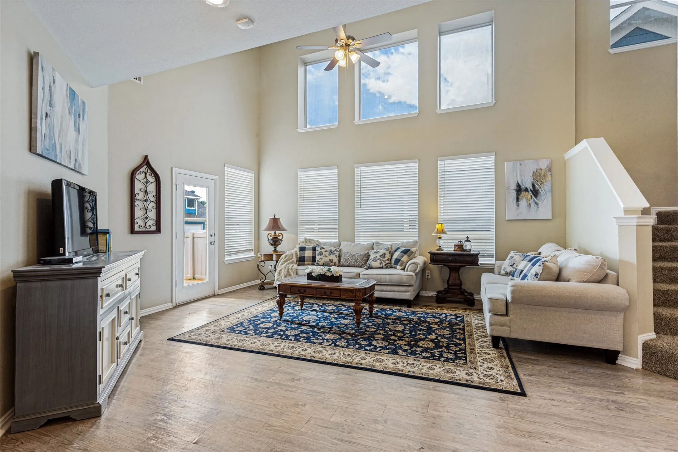 Two-story living area with high ceilings, wood-finish flooring, recessed lighting, and multiple large windows