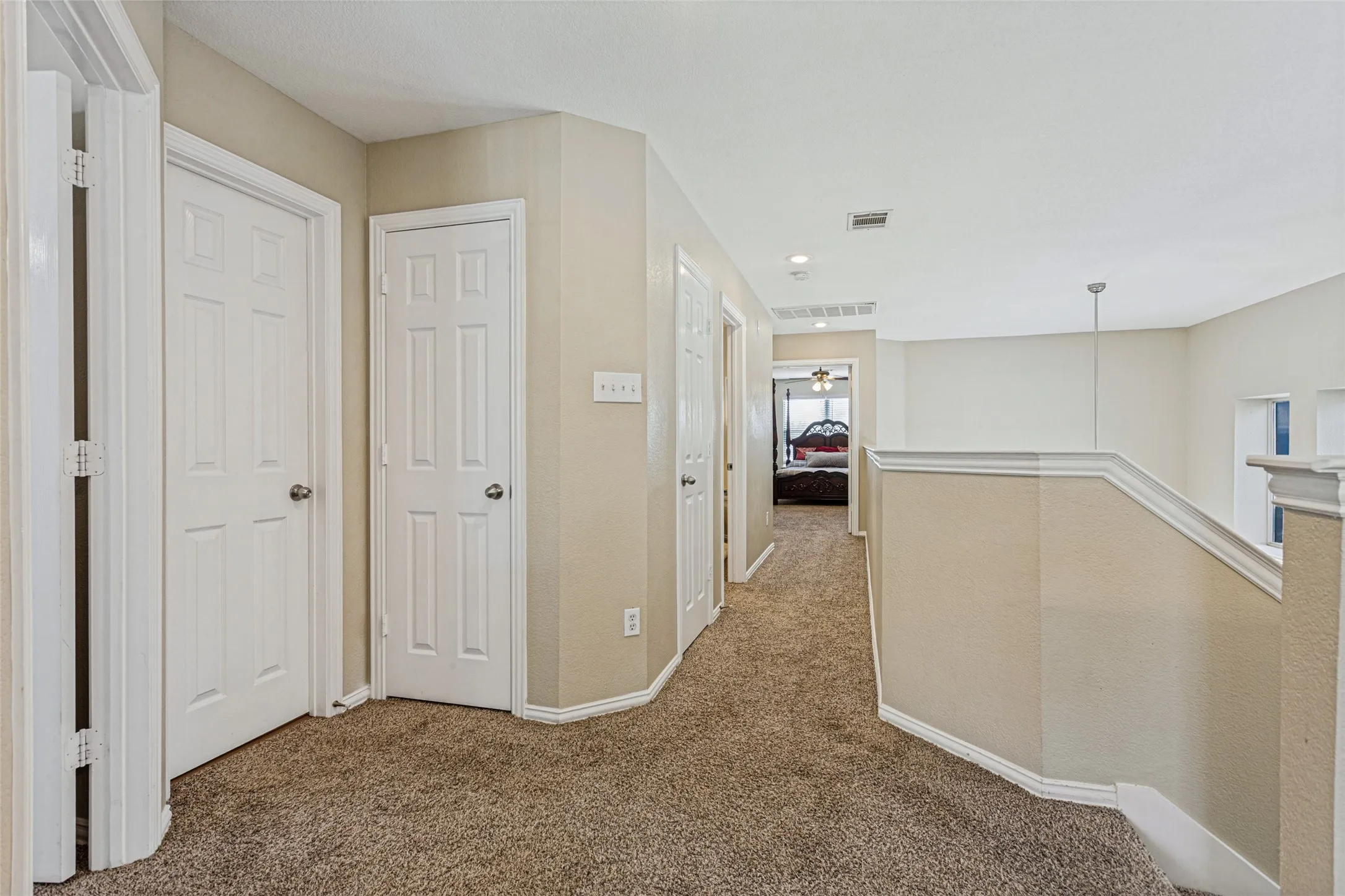 Carpeted hallway with white interior doors, recessed lighting, and a painted banister with white trim