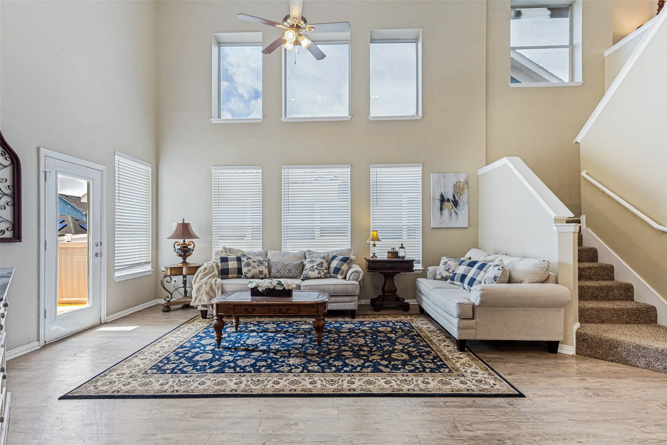Two-story living area with high ceilings, multiple windows, a ceiling fan, and wood-finish flooring