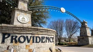 Stone entry monument featuring an arched metal accent with decorative lighting