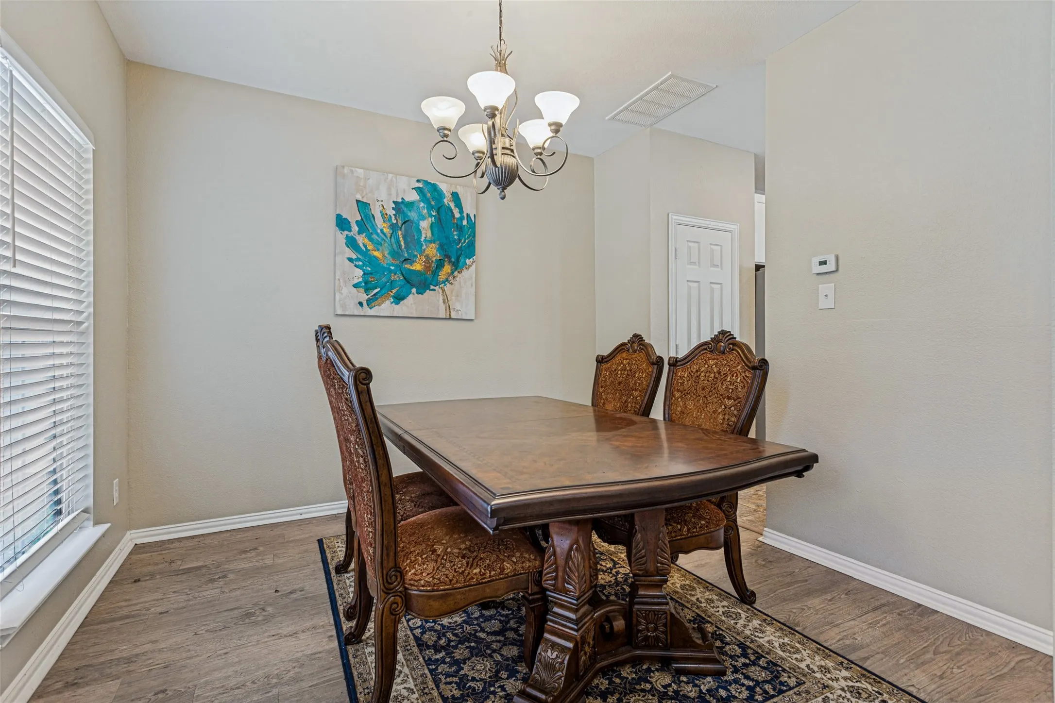 Dining area featuring wood-finish flooring, a window with blinds, and an overhead chandelier