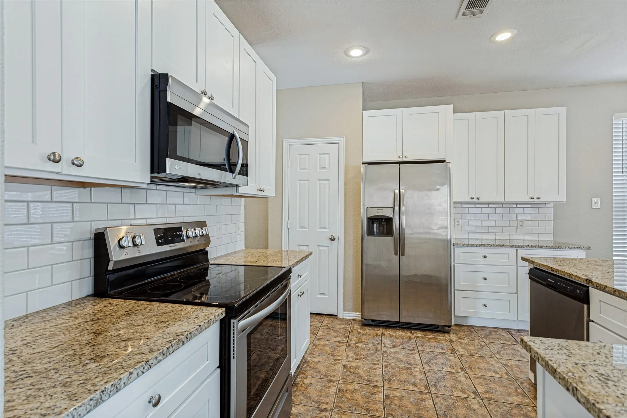 Kitchen featuring white shaker cabinetry, stainless steel appliances, speckled countertops, subway tile backsplash, and tile flooring