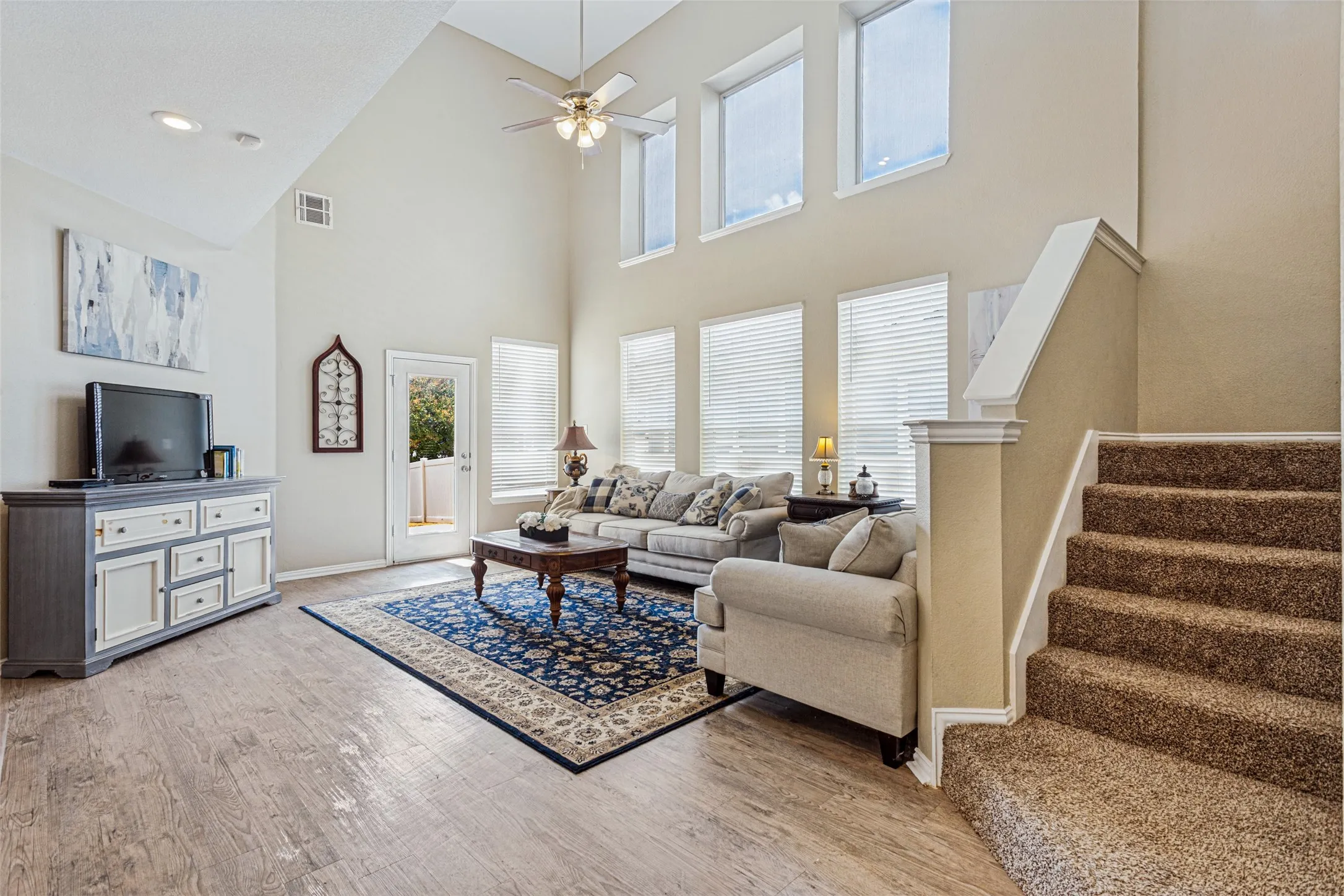 Vaulted ceiling with a ceiling fan, multiple windows, wood-finish flooring, and a carpeted staircase