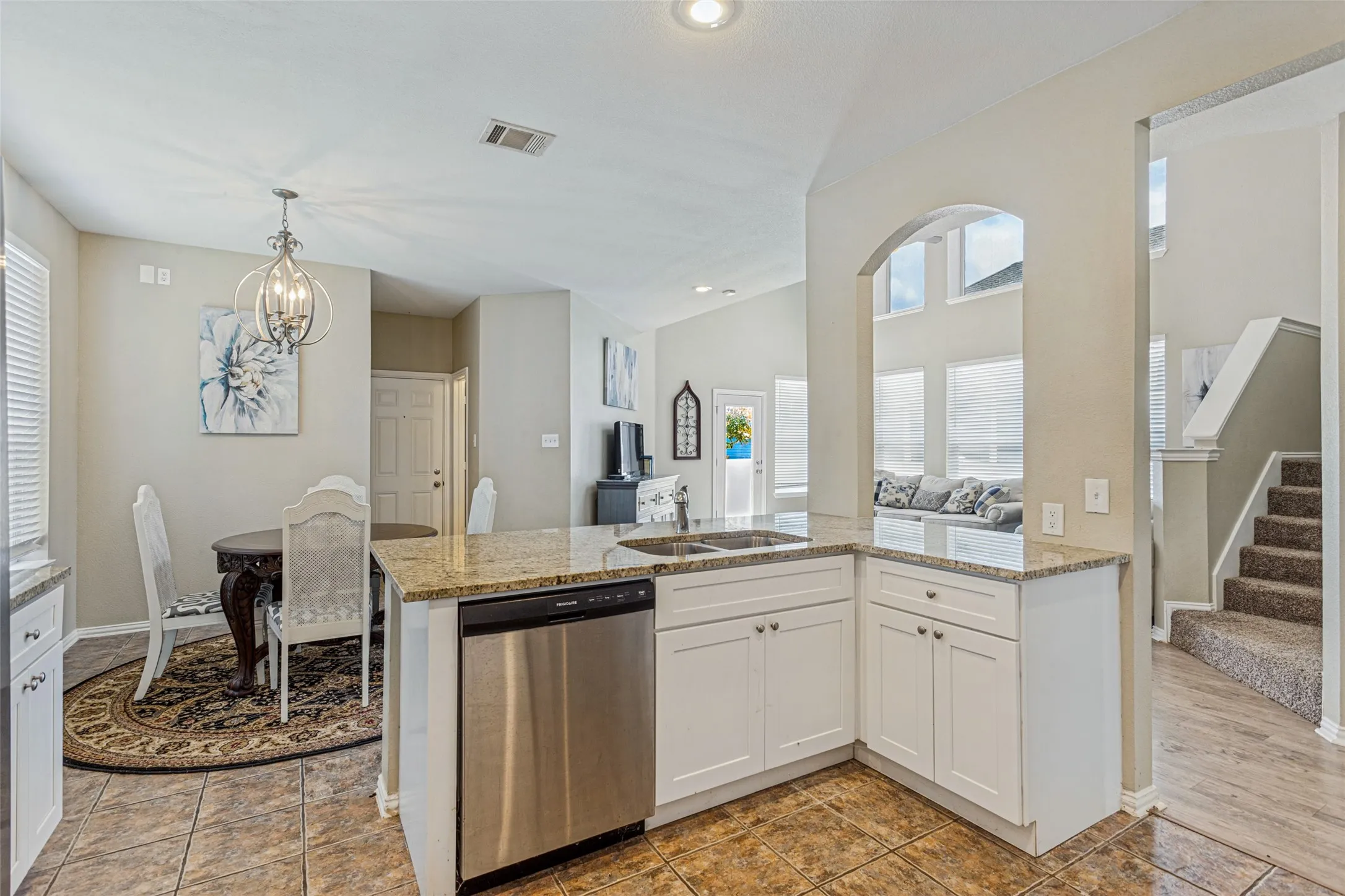 Kitchen featuring granite-style countertops, stainless steel dishwasher, white cabinetry, and tile flooring