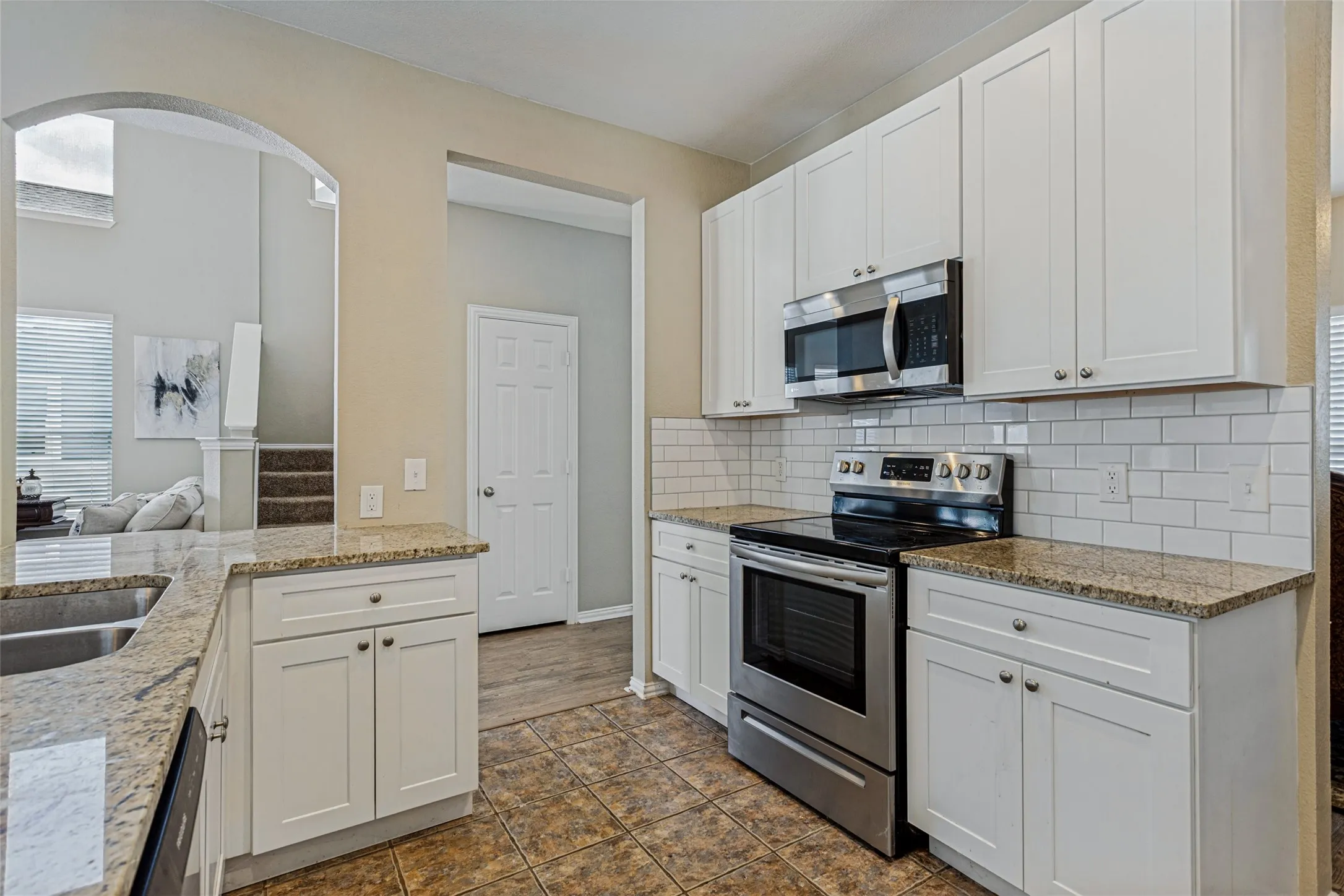 White shaker cabinetry, stainless steel appliances, subway tile backsplash, granite countertops, and tile flooring