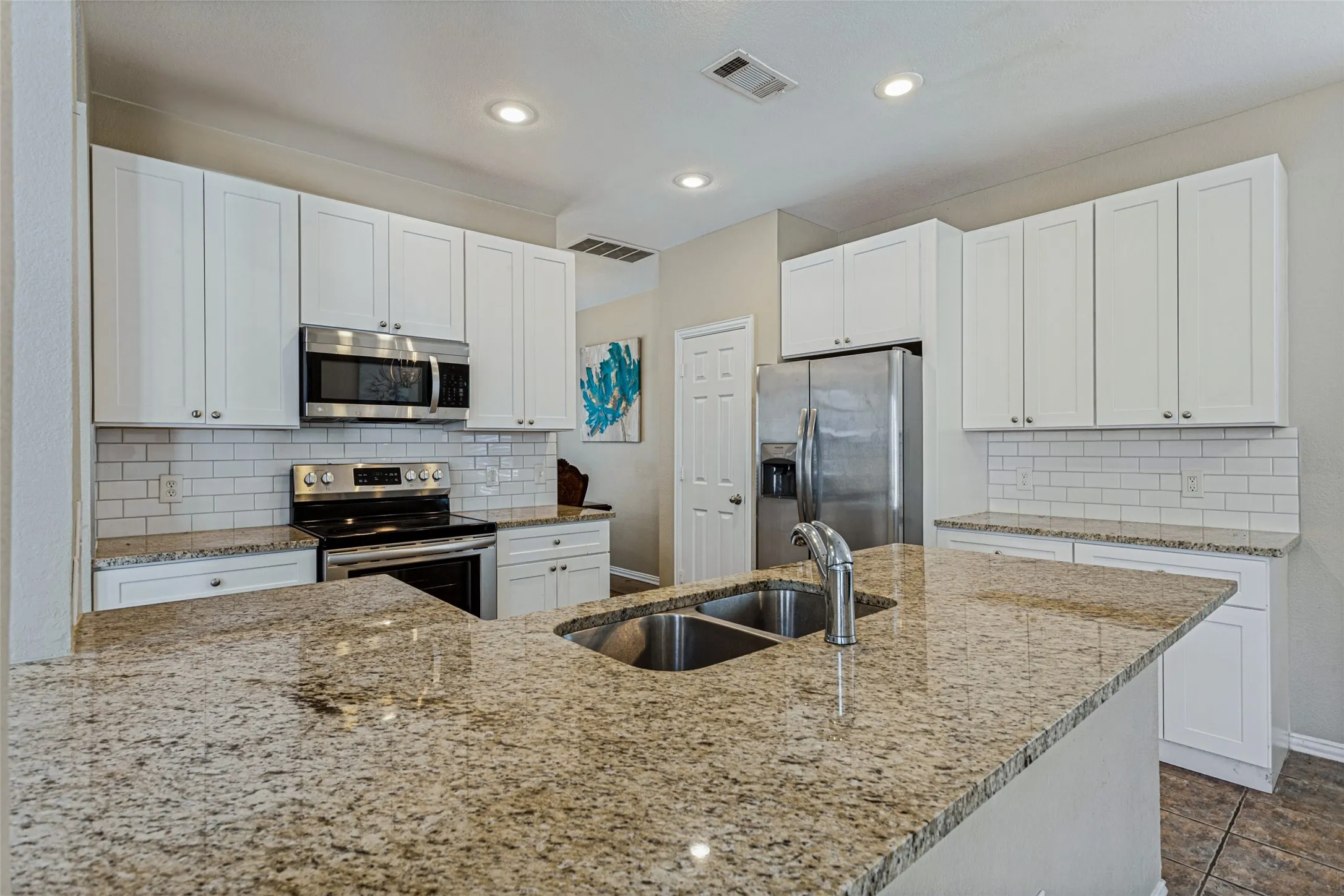 Kitchen featuring an island with a dual basin sink, stainless steel appliances, white subway tile backsplash, and white cabinetry