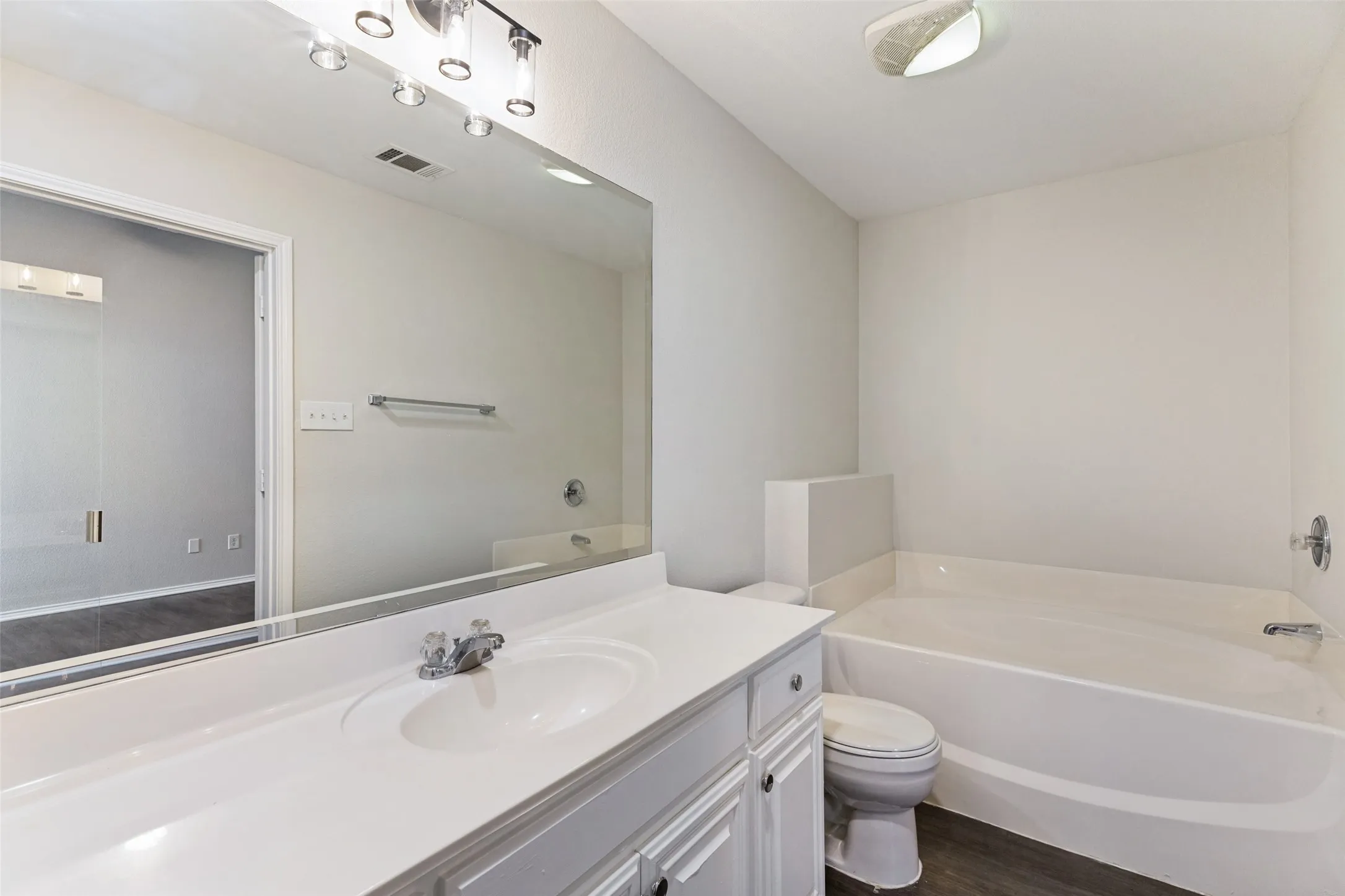 Single vanity with integrated sink, white cabinetry, a large wall-mounted mirror, a tub, and wood-finish flooring