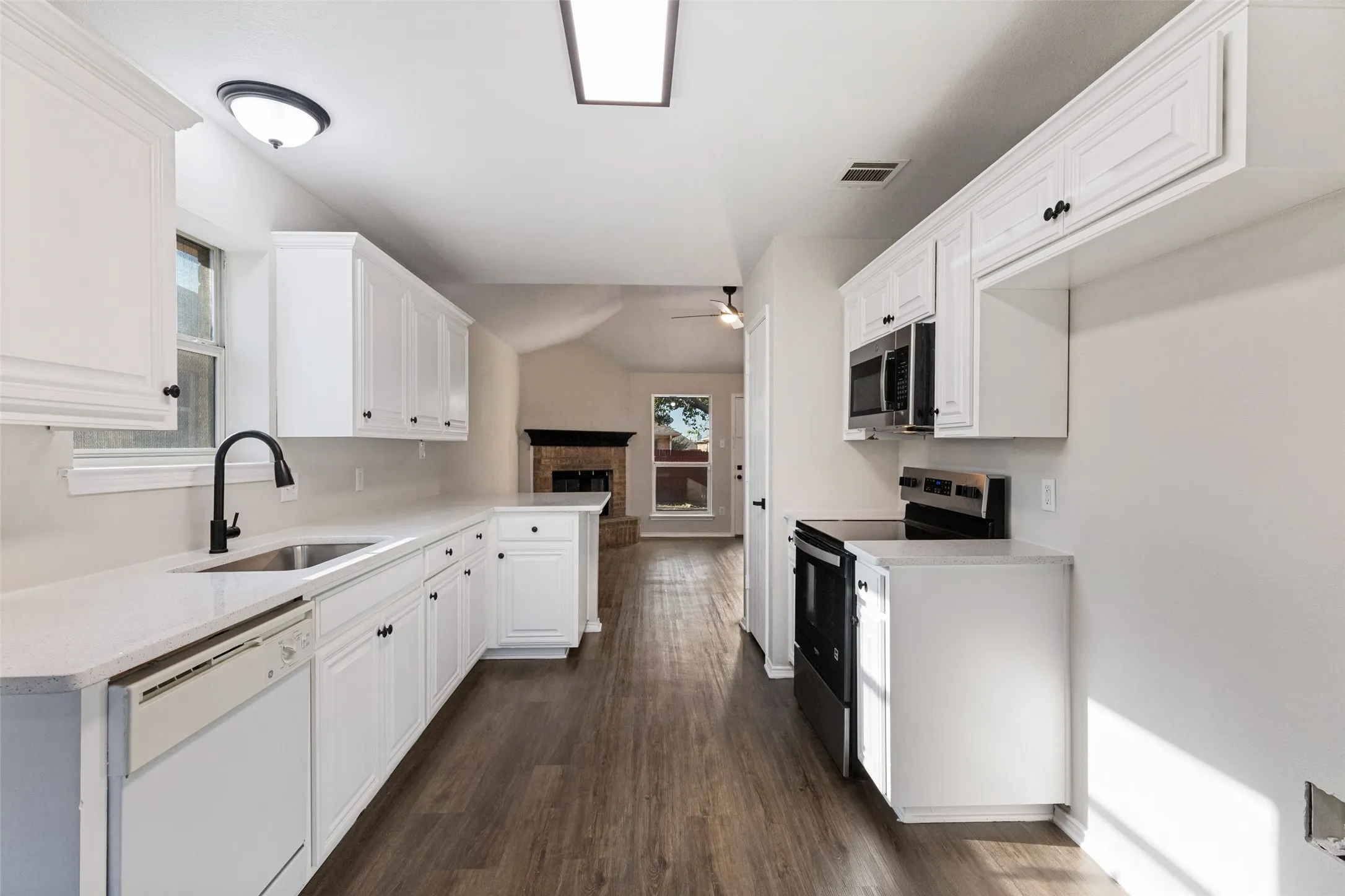 White cabinetry with black hardware, wood-finish flooring, stainless steel sink with black faucet, built-in microwave, and a black electric range