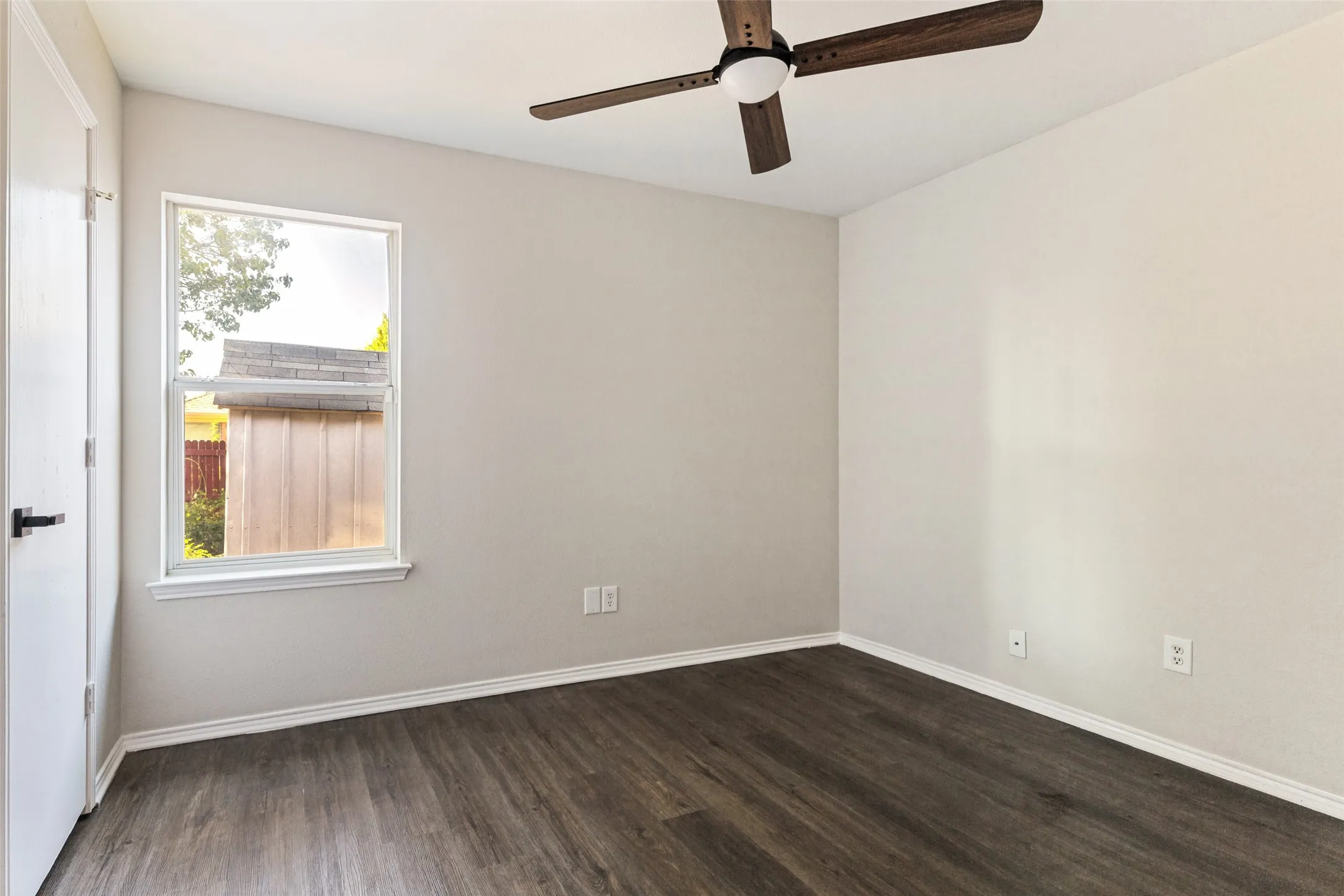 Wood-finish flooring, white trim, ceiling fan with integrated lighting, and a single window