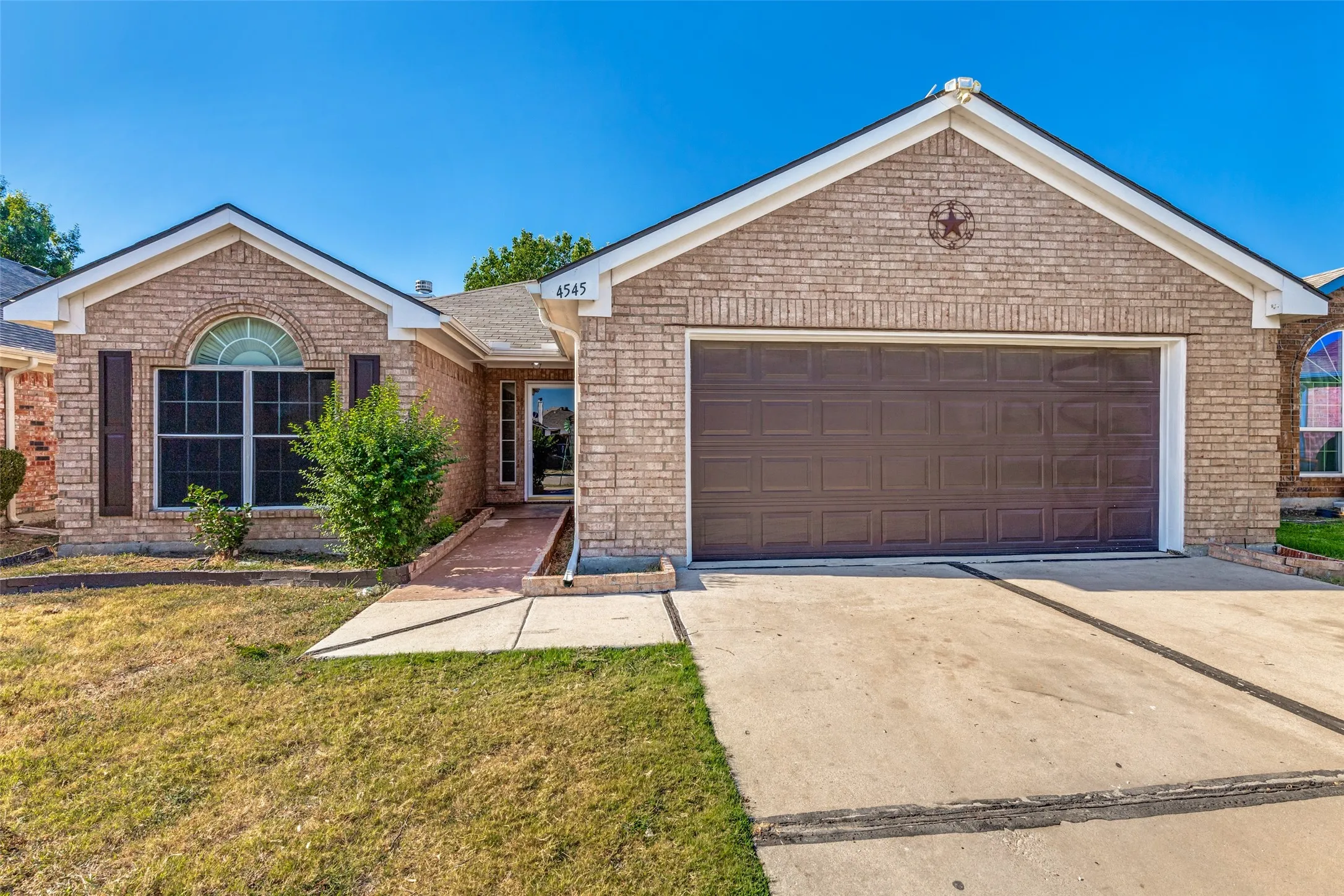Brick exterior with an attached garage, arched window, and concrete driveway