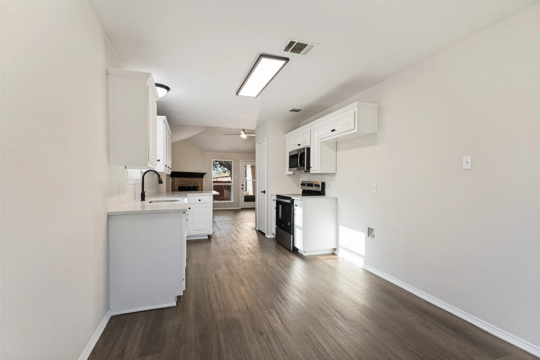 Wood-finish flooring throughout, white cabinetry, integrated microwave, stainless steel range, and a ceiling fan in the background