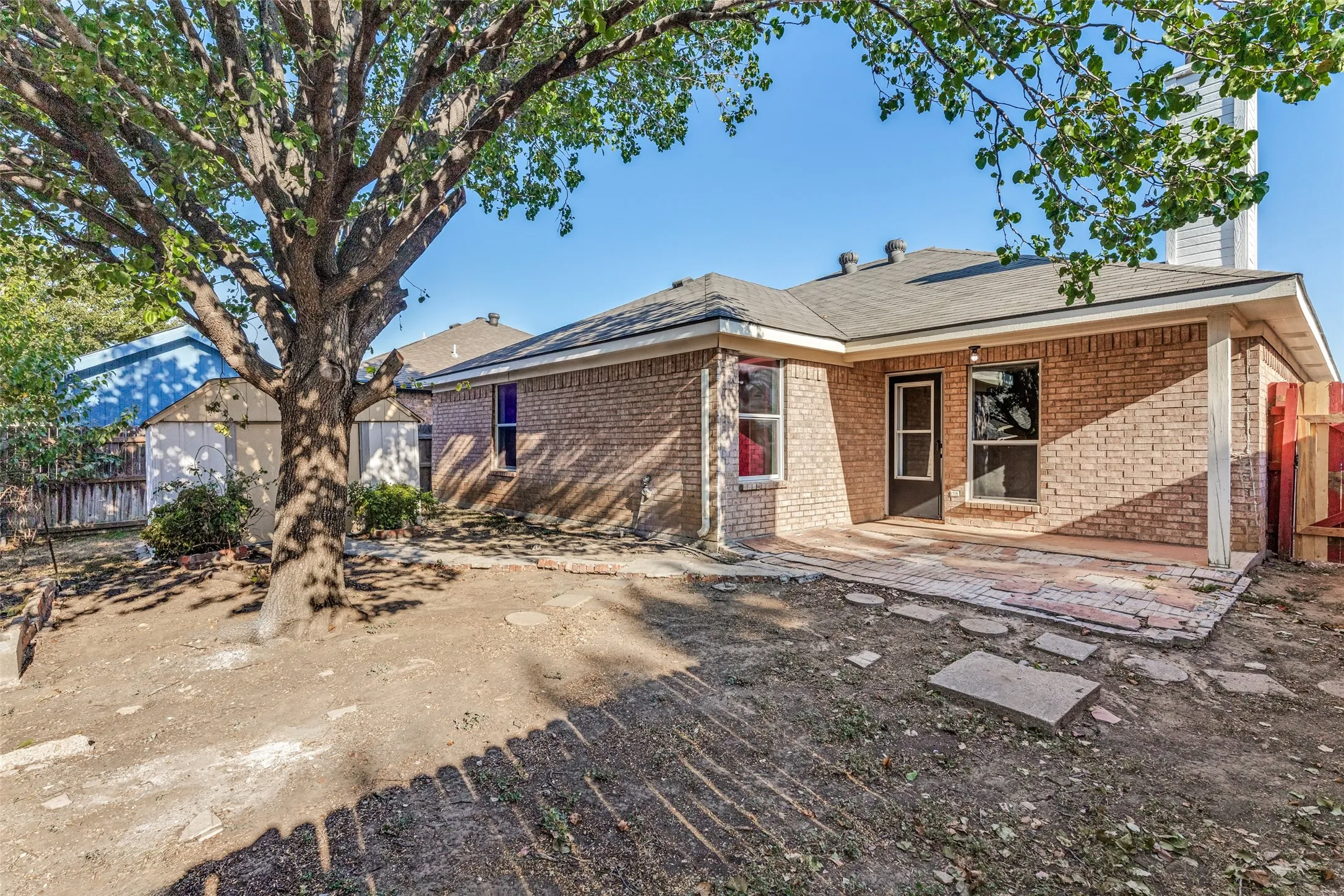 Brick exterior with a covered patio, featuring a large mature tree and a detached storage shed