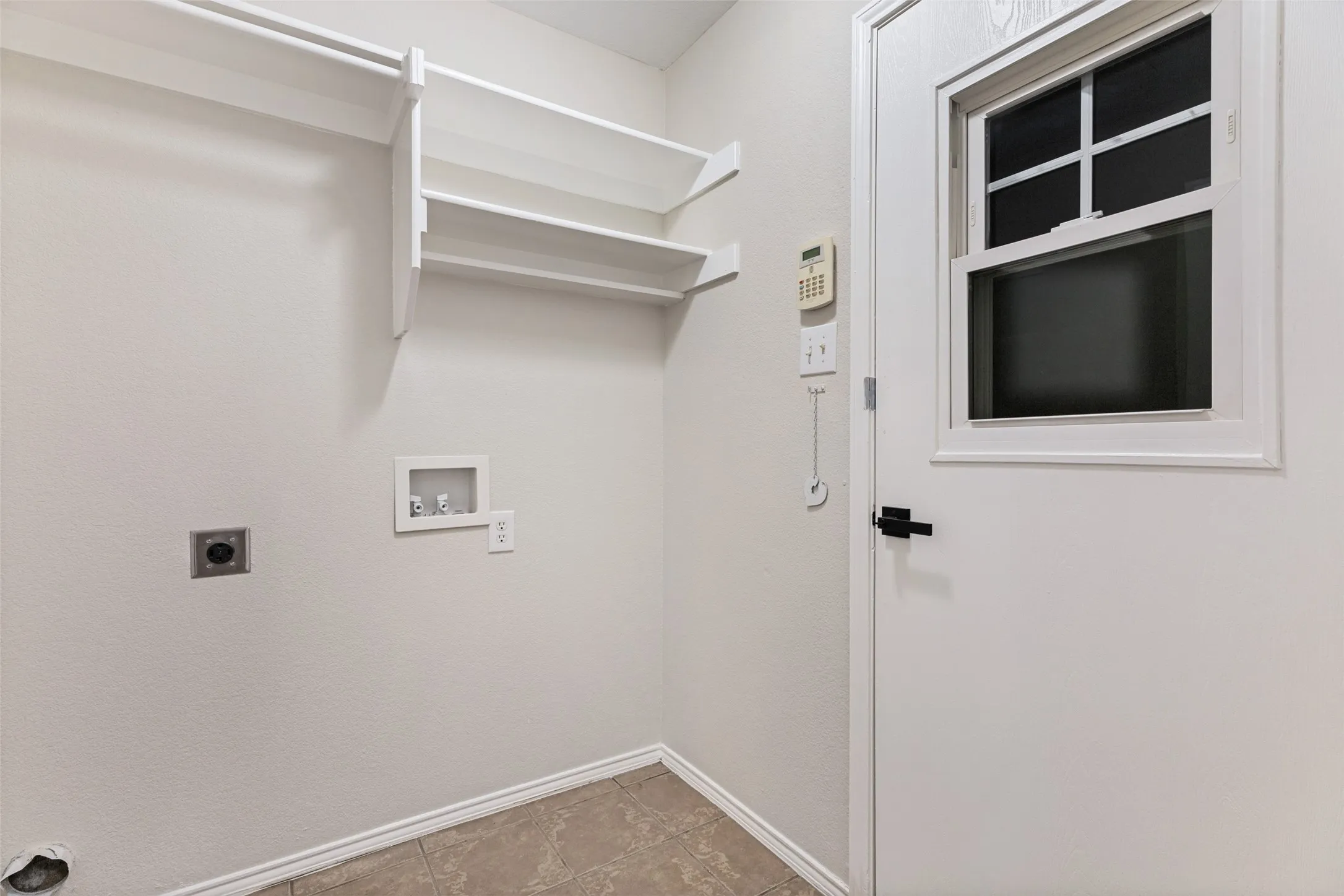 Built-in shelving, hanging rod, white paneled door with window, black hardware, and tiled flooring