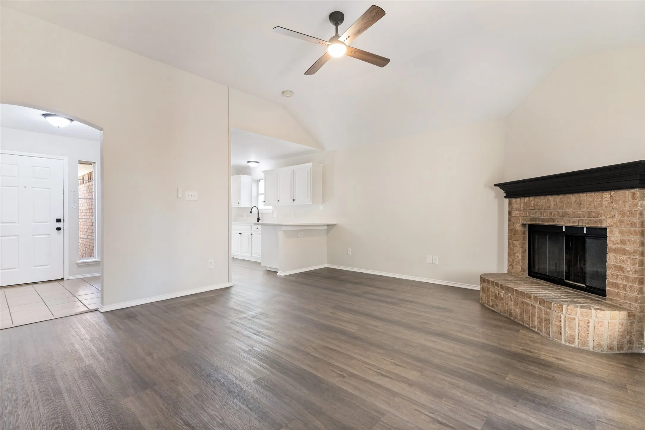 Wood-finish flooring, vaulted ceiling, and a brick fireplace with a dark mantel