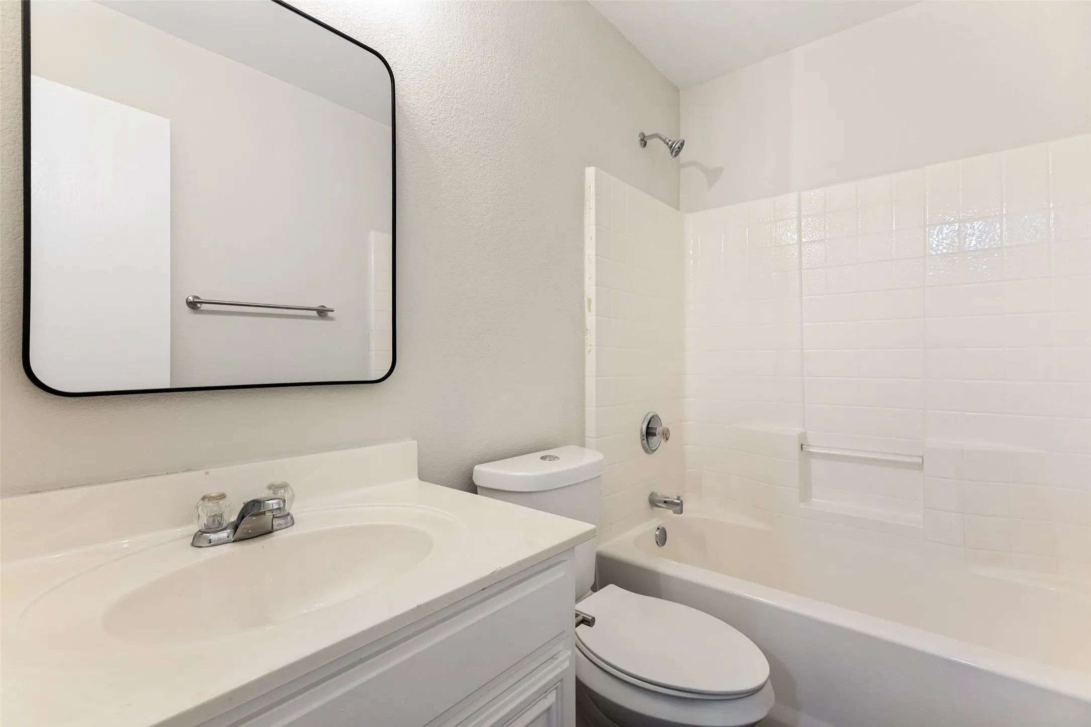 White tile shower surround, integrated bathtub, and white vanity with an integrated sink
