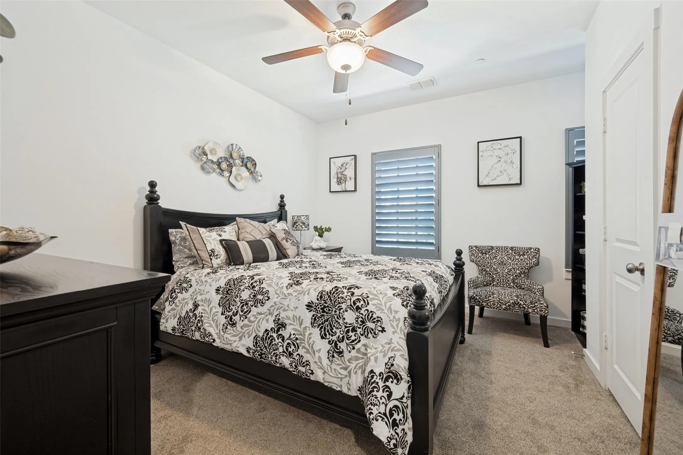 Carpeted room featuring a ceiling fan, window with plantation shutters, built-in shelving, and a white paneled door