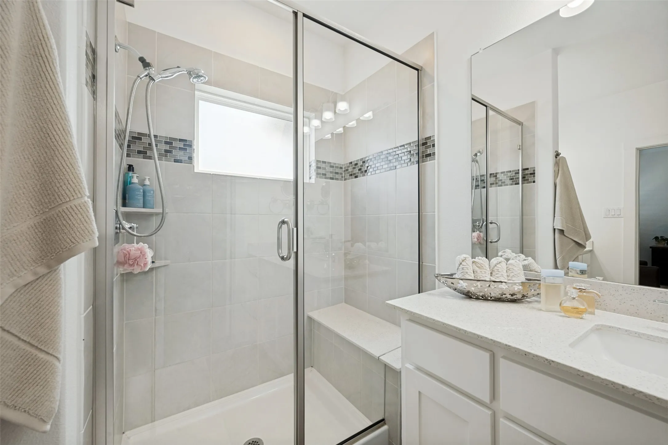 Glass-enclosed shower with a built-in bench, tile surround, and mosaic accent band