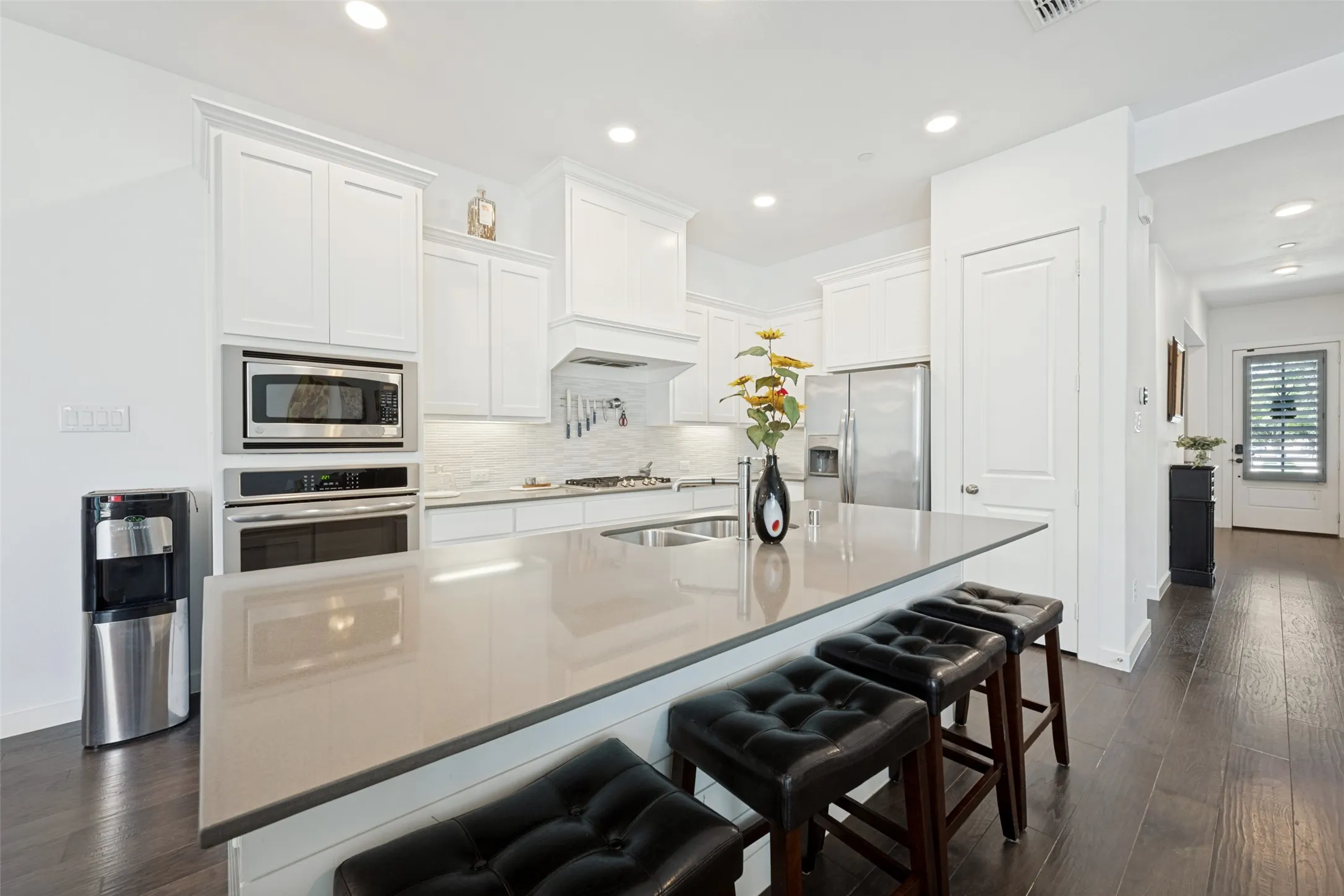 Kitchen featuring white cabinetry, built-in stainless steel appliances, a large center island with counter seating, and dark wood-finish flooring