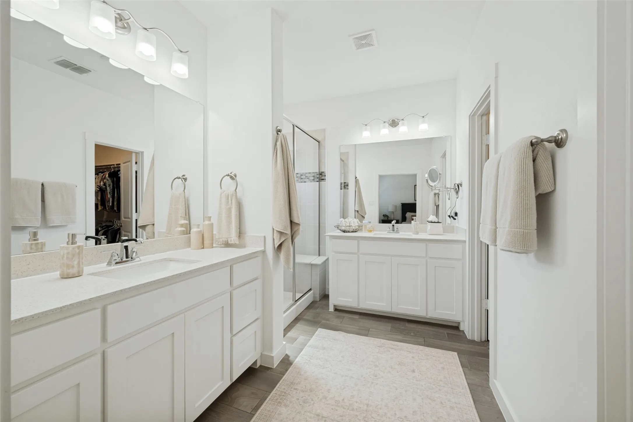 Dual vanity with white cabinetry, light-toned countertops, large mirrors, a walk-in shower, and wood-finish flooring