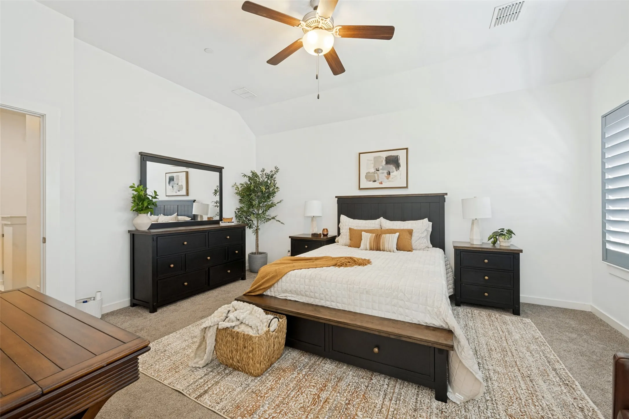 Vaulted ceiling with a ceiling fan, carpeted flooring, and window with plantation shutters