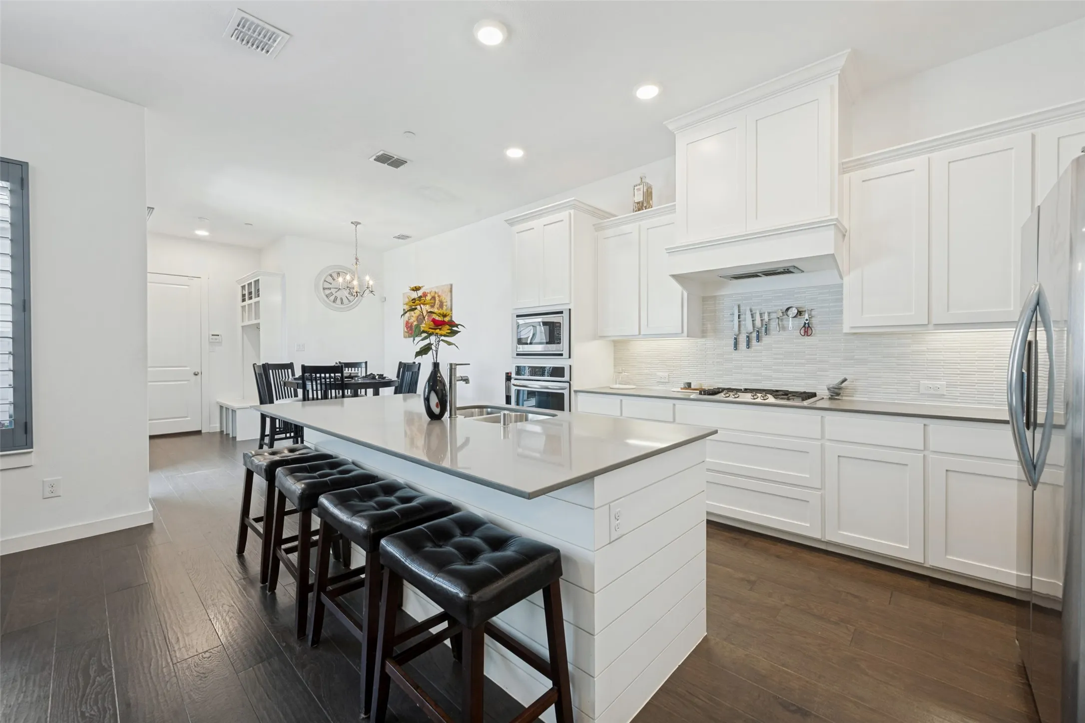 Gourmet kitchen with white cabinetry, built-in double ovens, a gas cooktop, and an expansive central island with counter seating