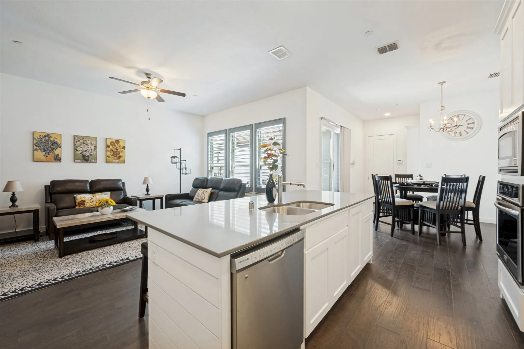 Open-concept living space featuring wood-finish flooring, a kitchen island with an integrated sink, built-in stainless steel appliances, and a dining area with a chandelier