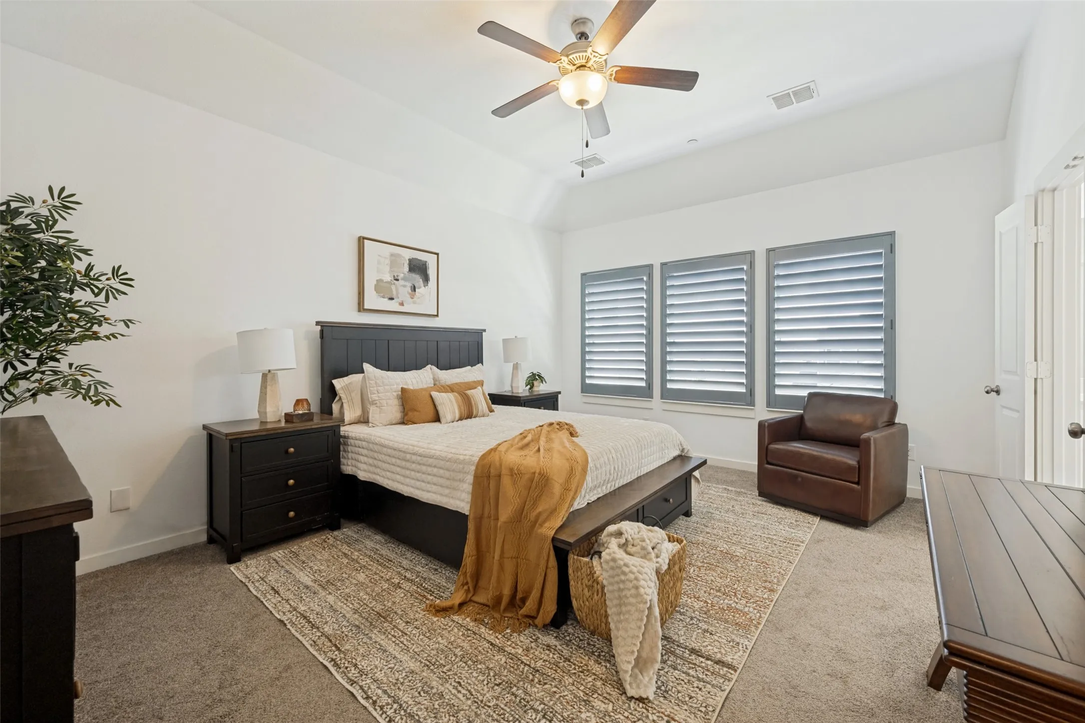 Vaulted ceiling with a ceiling fan, three windows with plantation shutters, and carpeted flooring