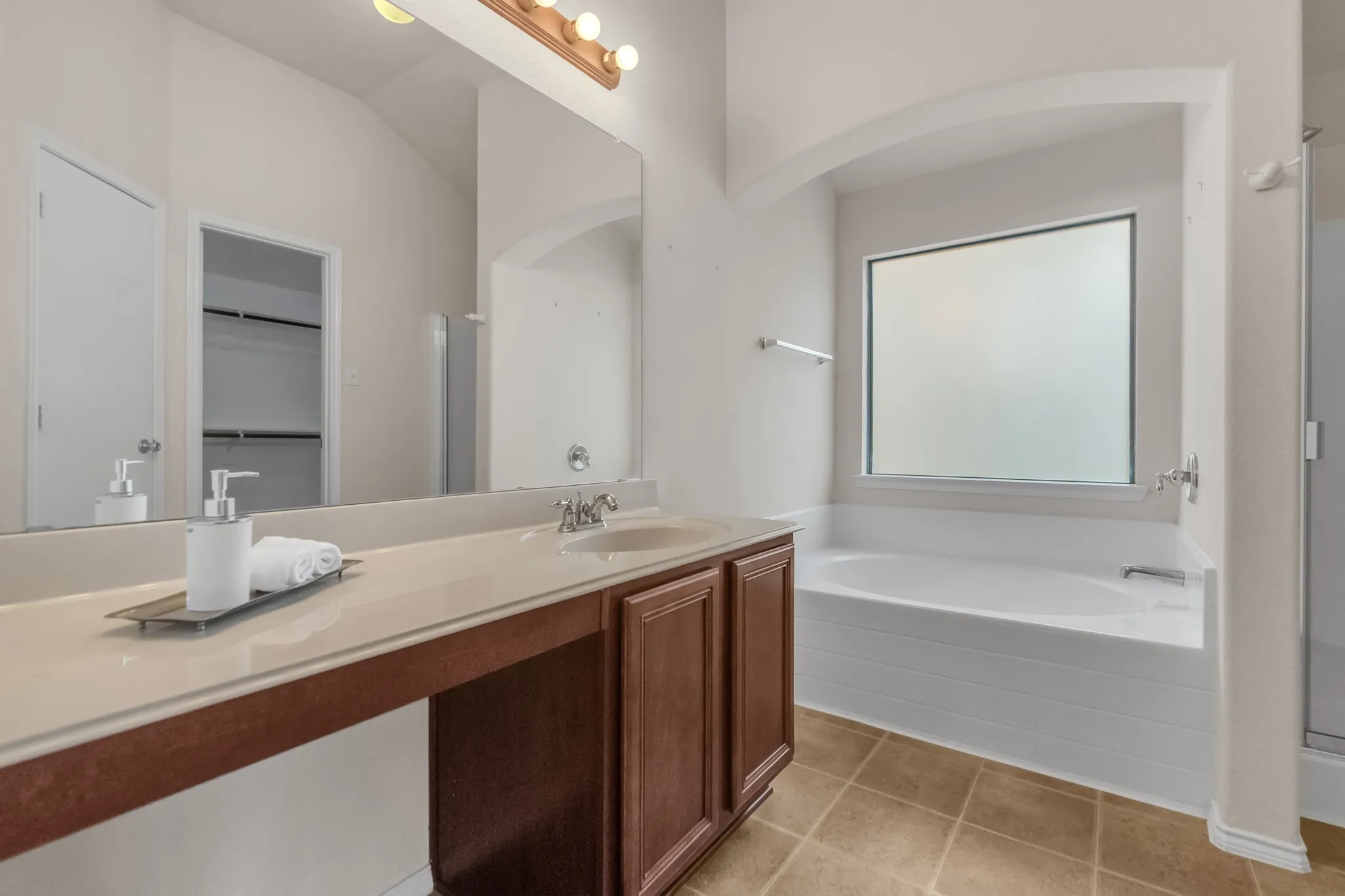 Dual vanity with a beige countertop, built-in soaking tub with tile surround, and an arched alcove