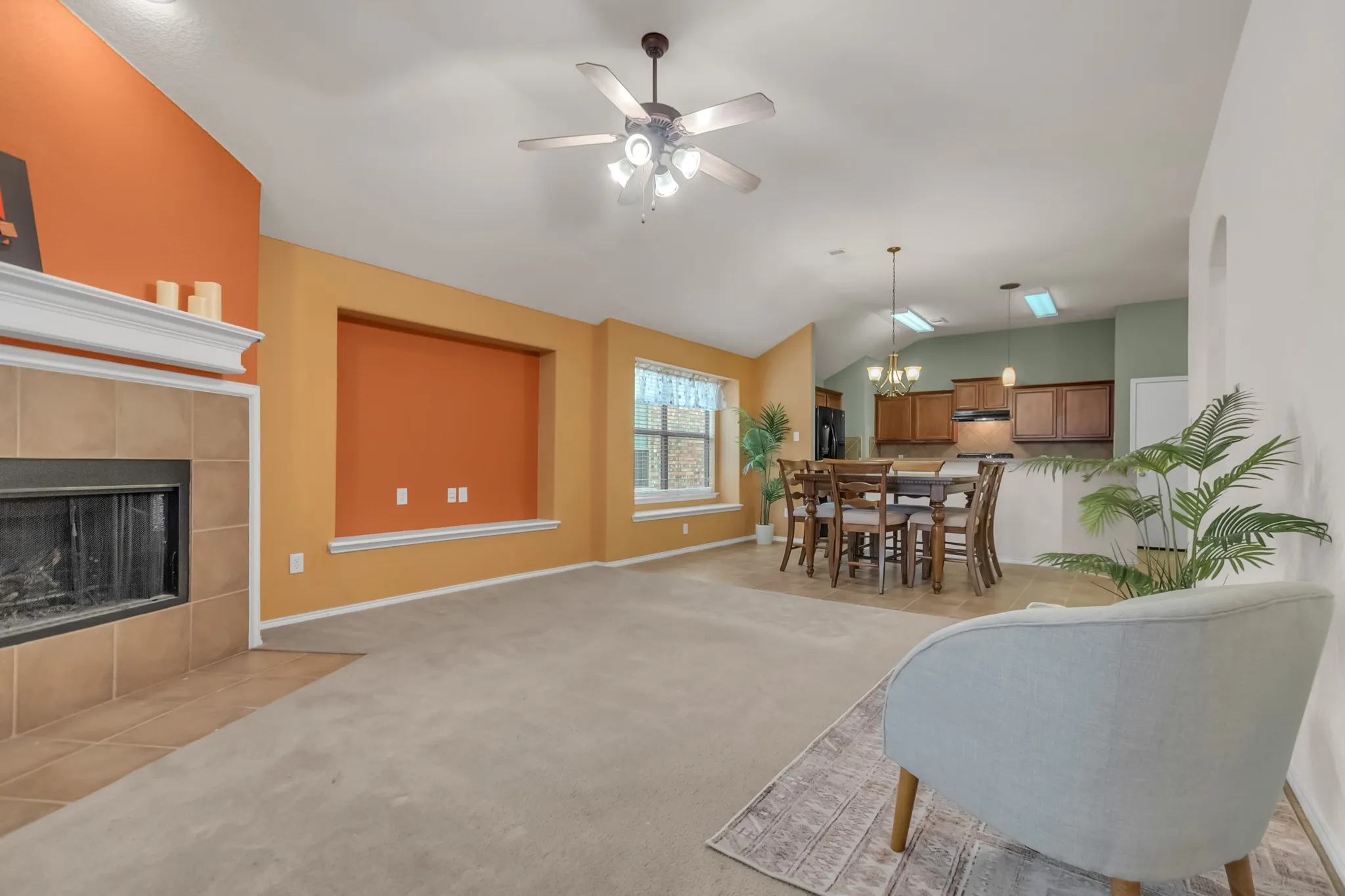 Vaulted ceiling living area featuring a tile-surround fireplace with mantel, recessed wall niche, and an open-concept dining space with a chandelier