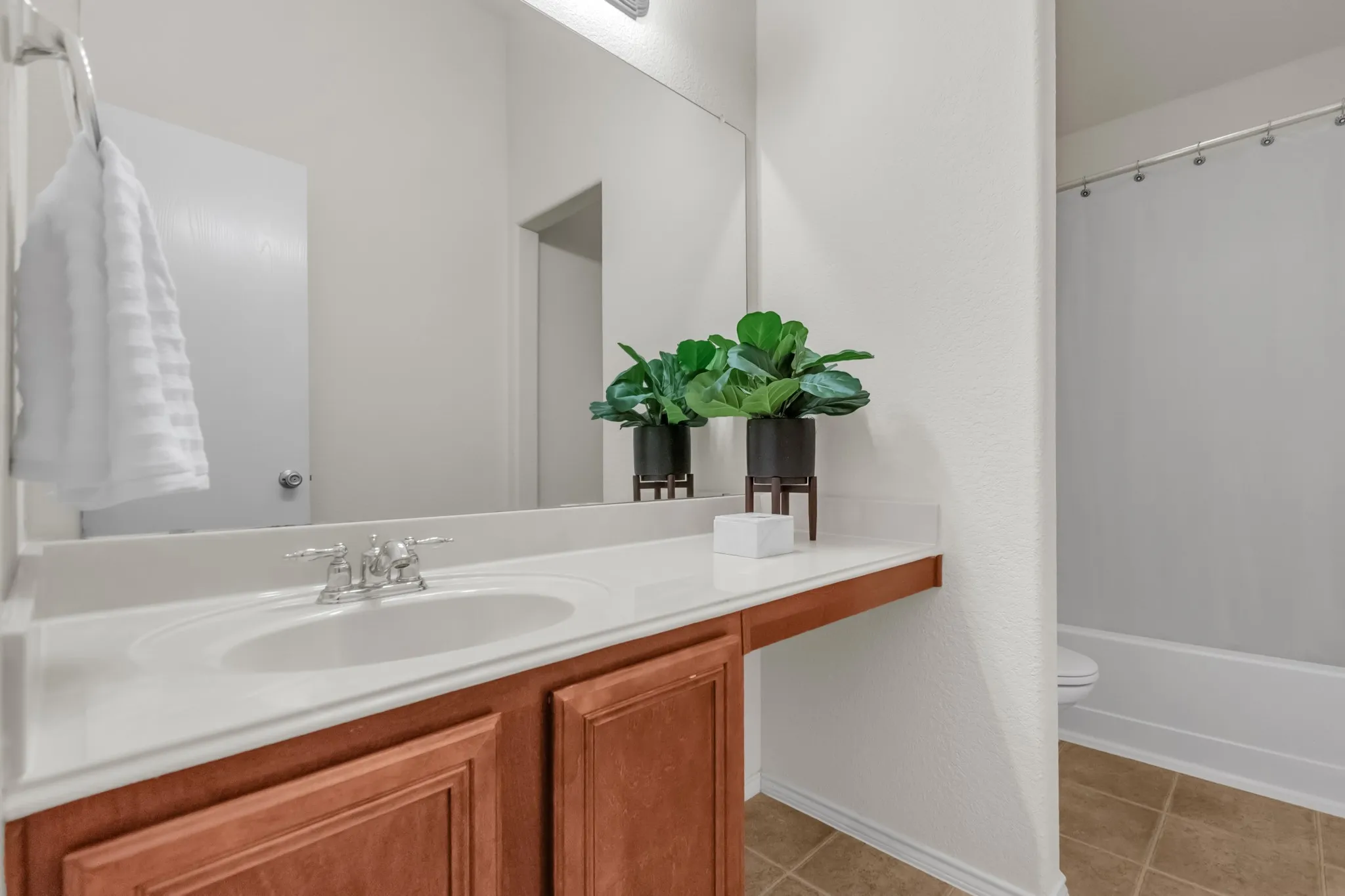 Vanity with a white countertop and integrated sink, chrome faucet, wood-finish cabinetry, and tiled flooring