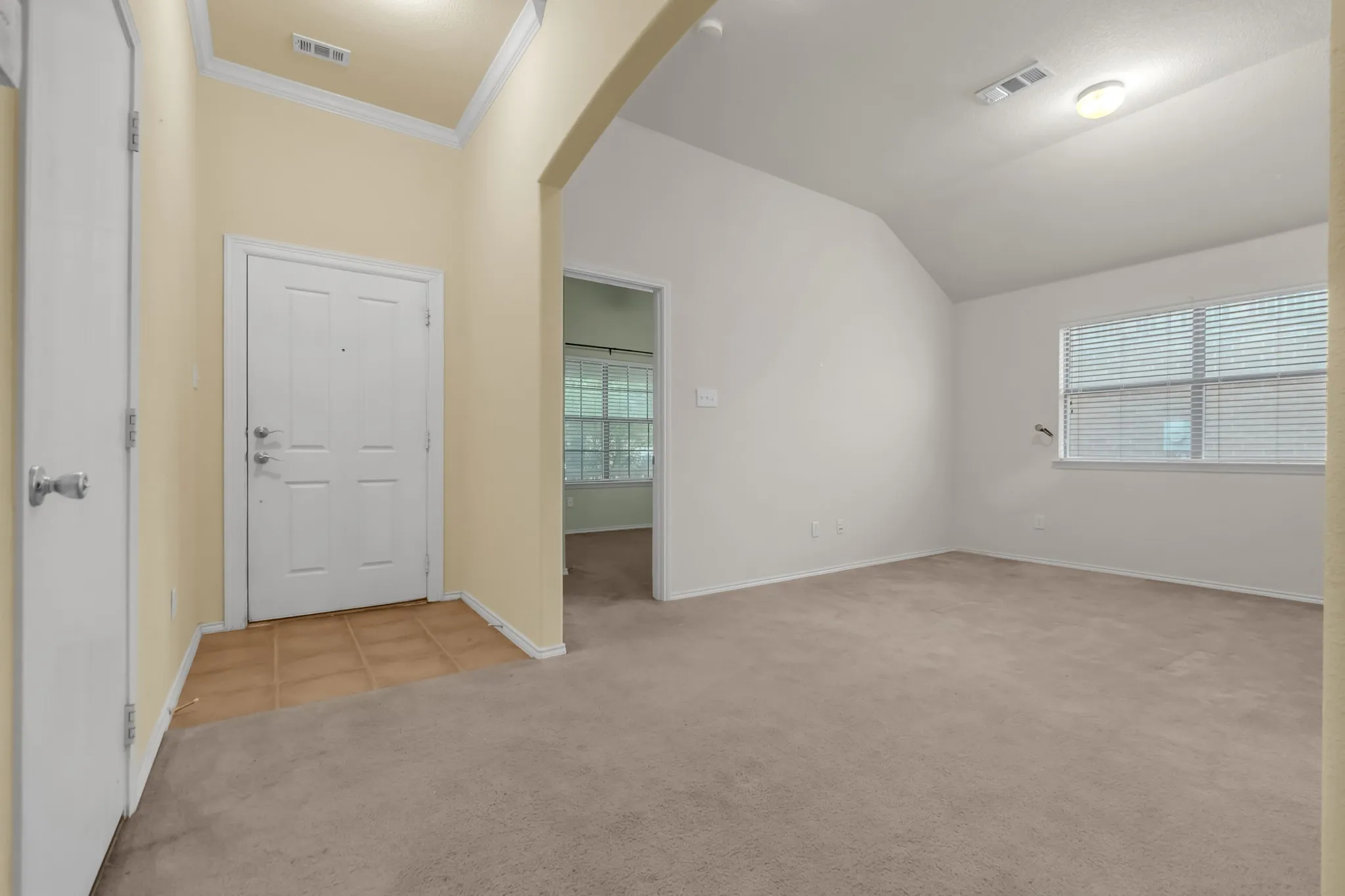 Vaulted ceiling, arched doorway, paneled interior door, tiled entry, and carpeted flooring