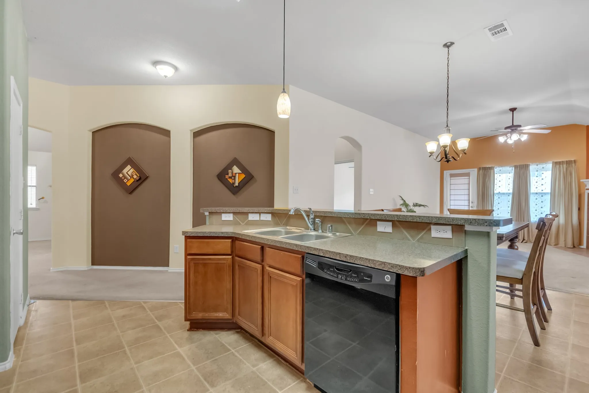 Kitchen featuring tile flooring, a dual basin sink, wood cabinetry, a black dishwasher, and a breakfast bar with a neutral countertop