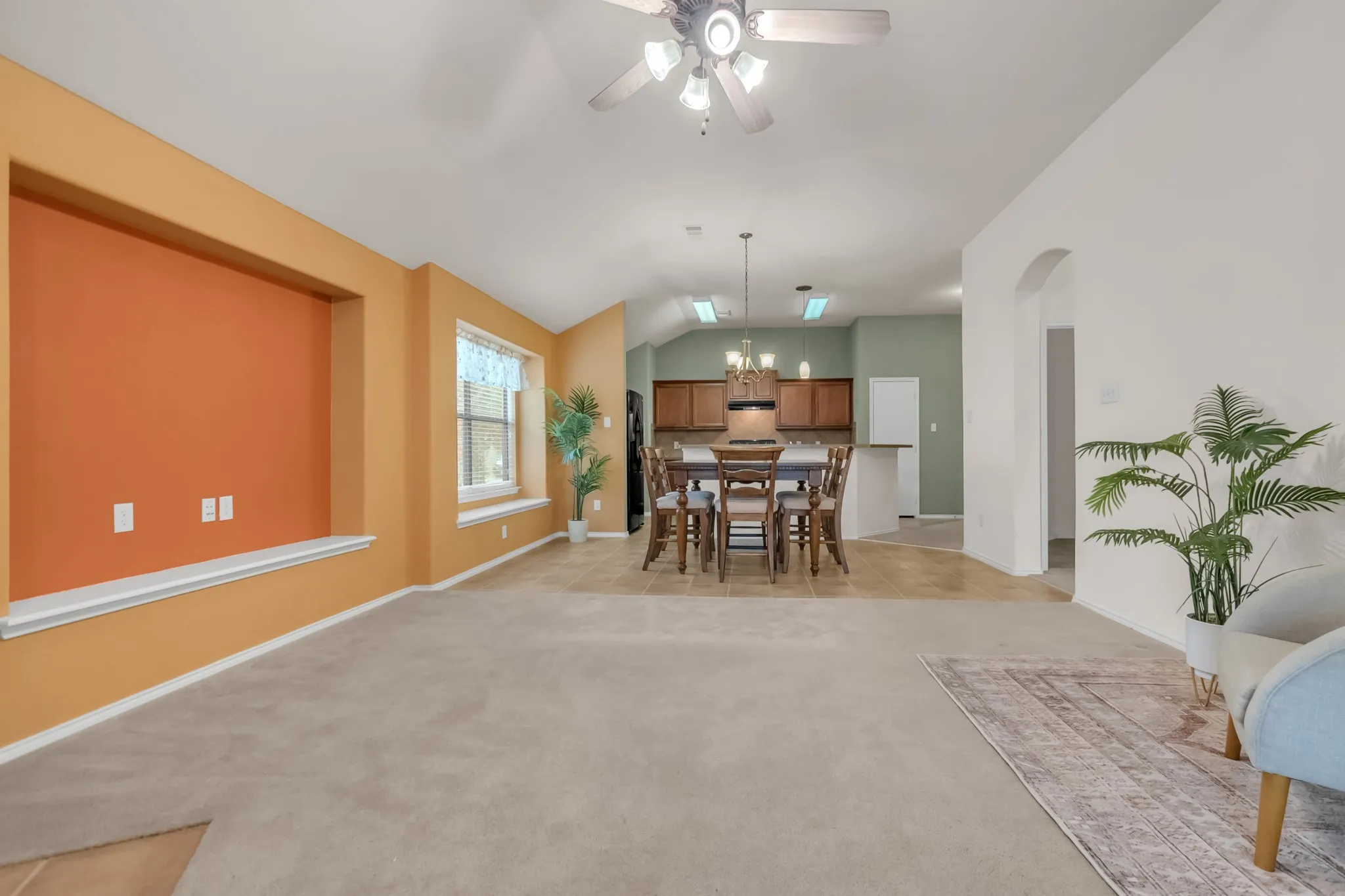 Open-concept living space featuring vaulted ceilings, carpeted flooring, a built-in wall niche, and an arched doorway