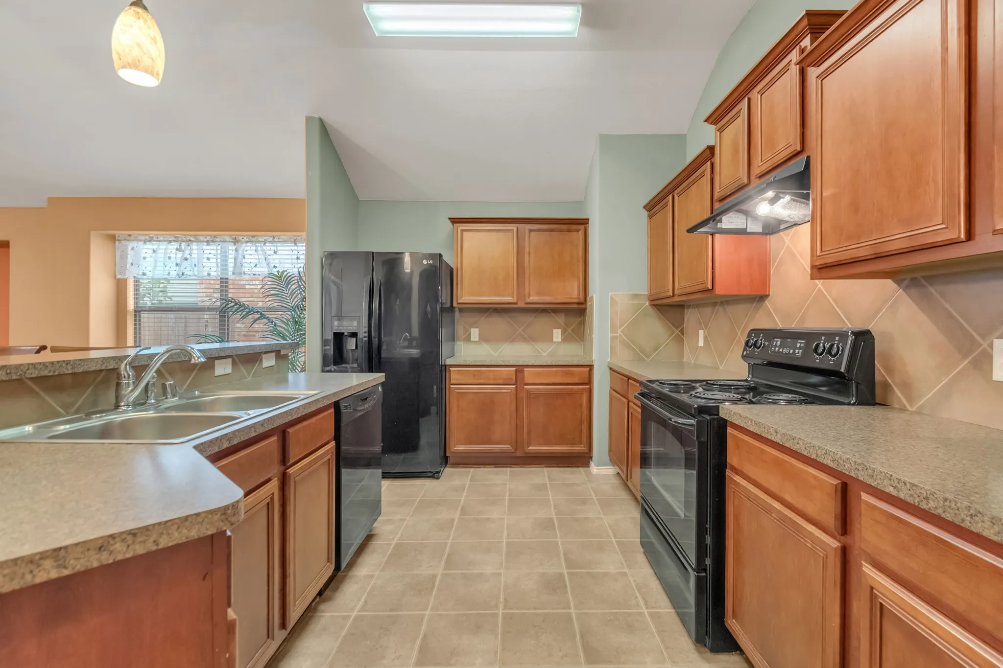 Kitchen featuring wood-finish cabinetry, tile flooring, black appliances, a double basin sink, and ample counter space
