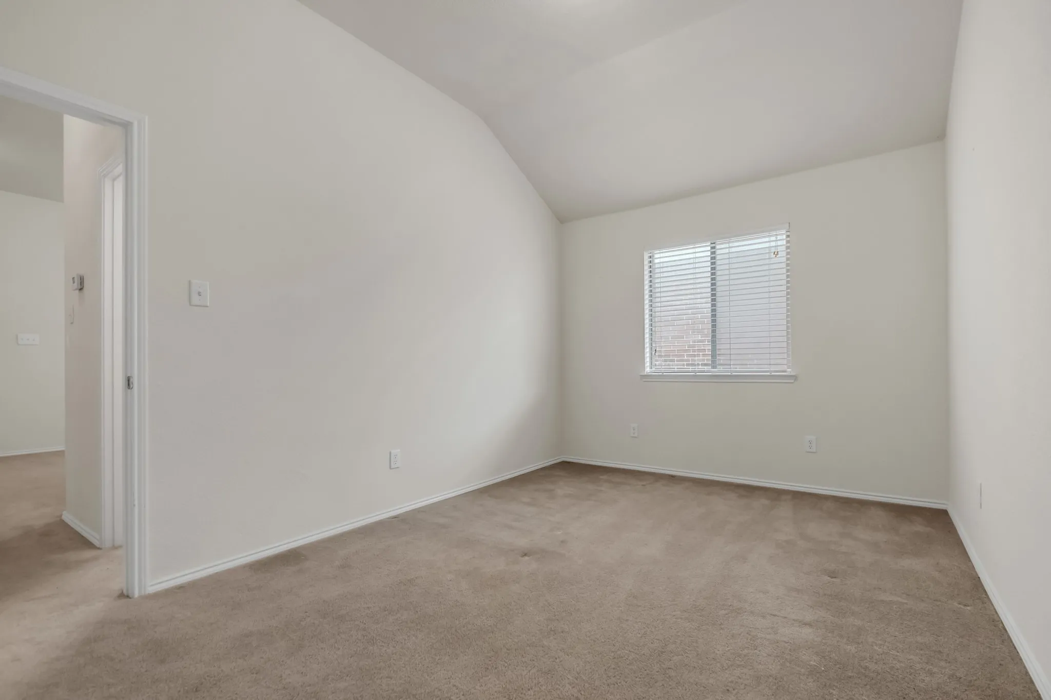 Vaulted ceiling, neutral wall paint, carpeted flooring, window with blinds, white trim