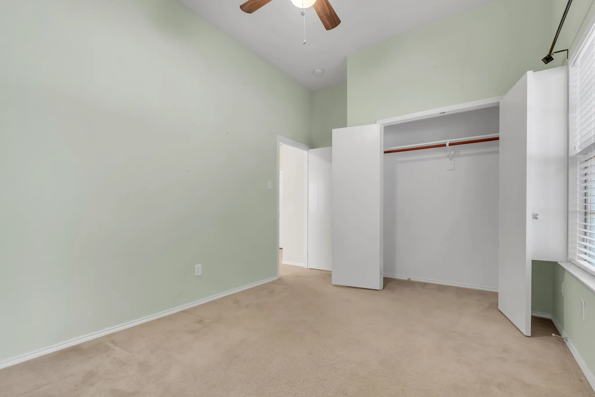 Vaulted ceiling with a ceiling fan, carpeted flooring, built-in closet with bi-fold doors, and a window with blinds